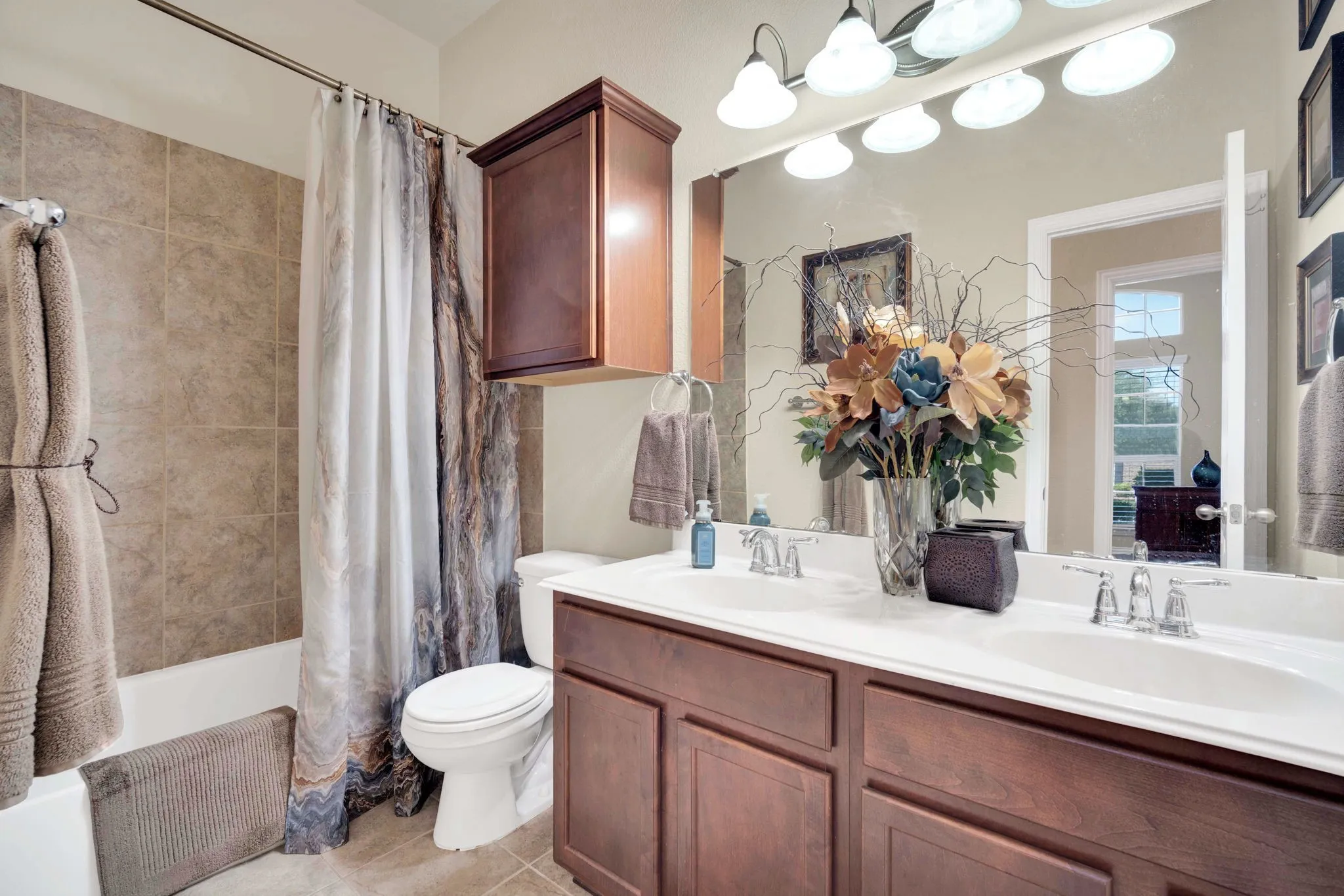 Bathroom featuring a dual-sink vanity with wood-finish cabinetry and chrome fixtures, a full-width mirror, and a multi-bulb vanity light