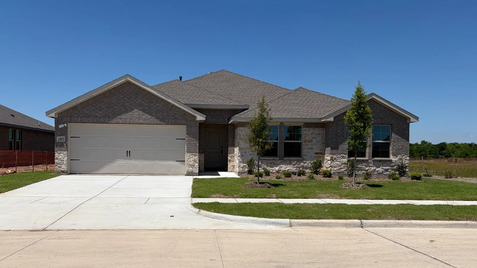 Front exterior featuring a brick and stone facade, a two-car garage, a concrete driveway, a sidewalk, and a manicured lawn with plantings
