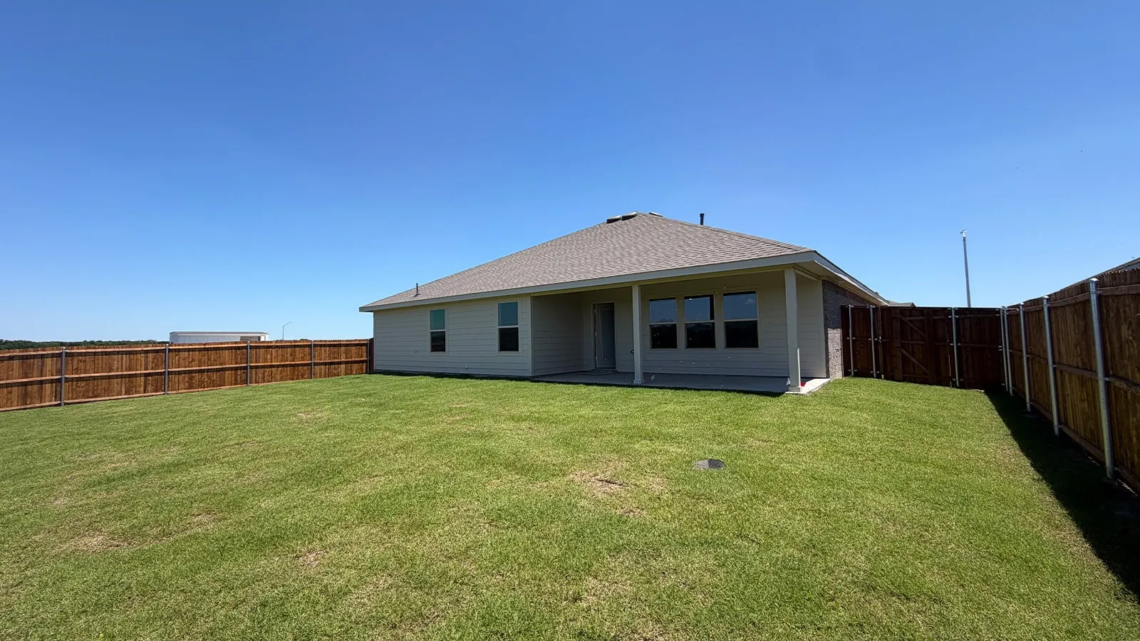 Expansive rear yard featuring a privacy fence, concrete patio, and a light-colored stucco exterior with multiple windows