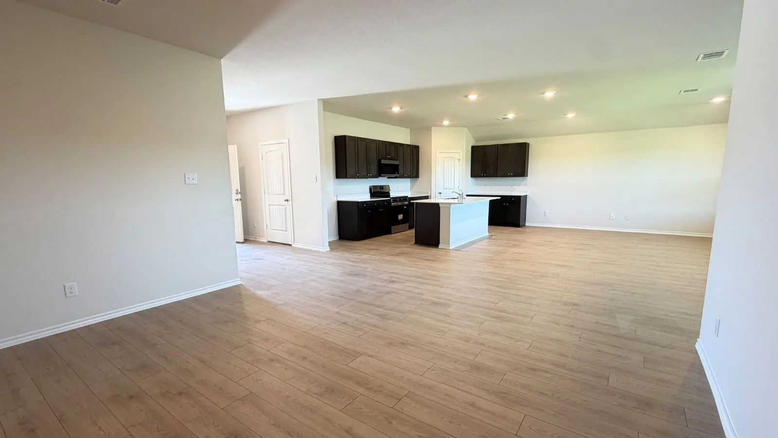 Expansive open-concept living area featuring wood-finish flooring, recessed lighting, and a kitchen island with a light-toned countertop
