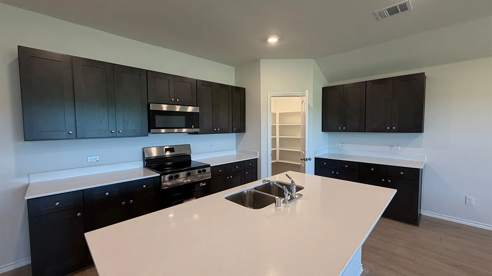 Contemporary kitchen featuring dark wood-finish cabinetry, stainless steel appliances, and a central island with a double basin sink