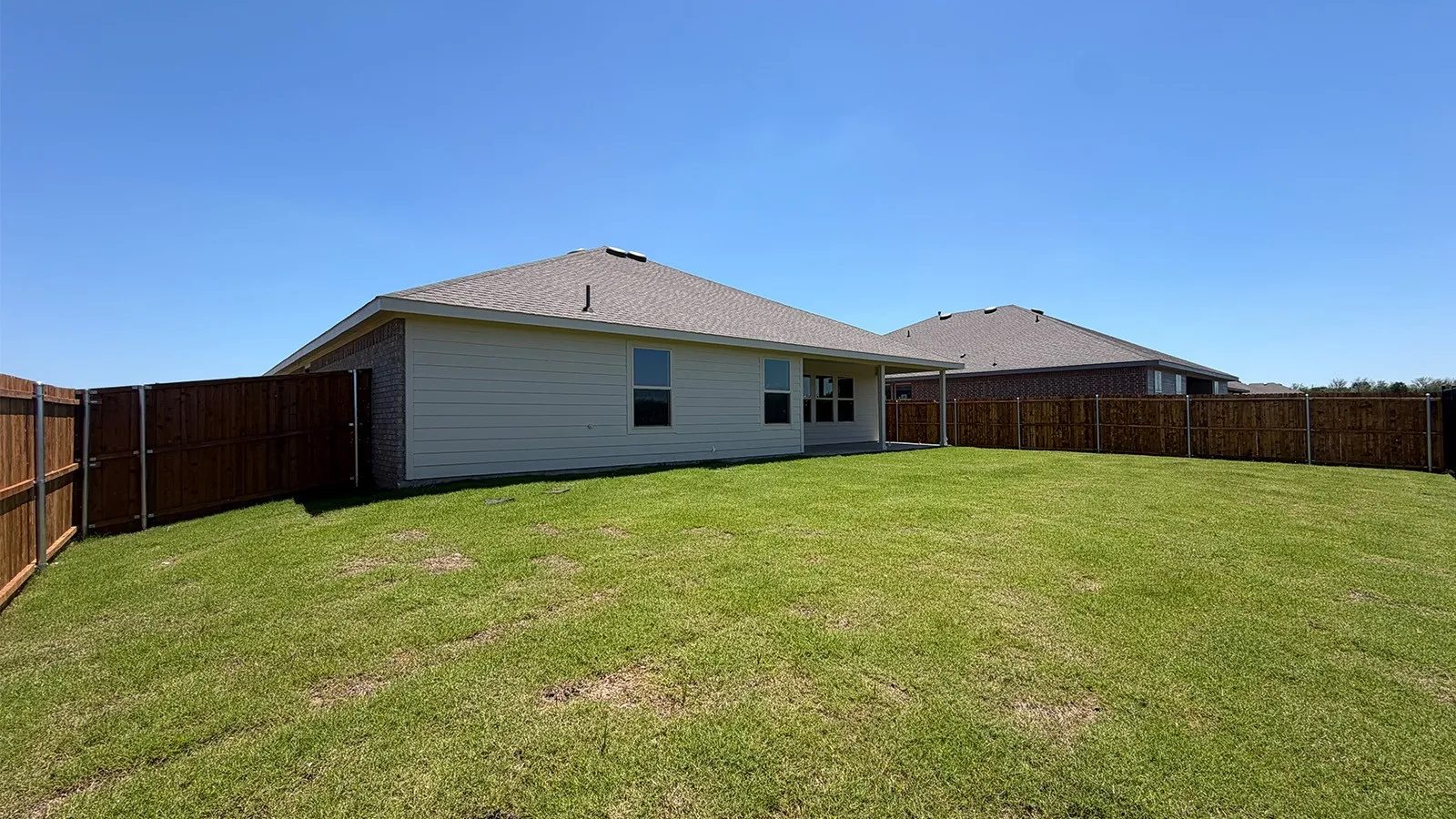 Expansive backyard featuring a manicured lawn, full privacy fencing, and a covered patio area