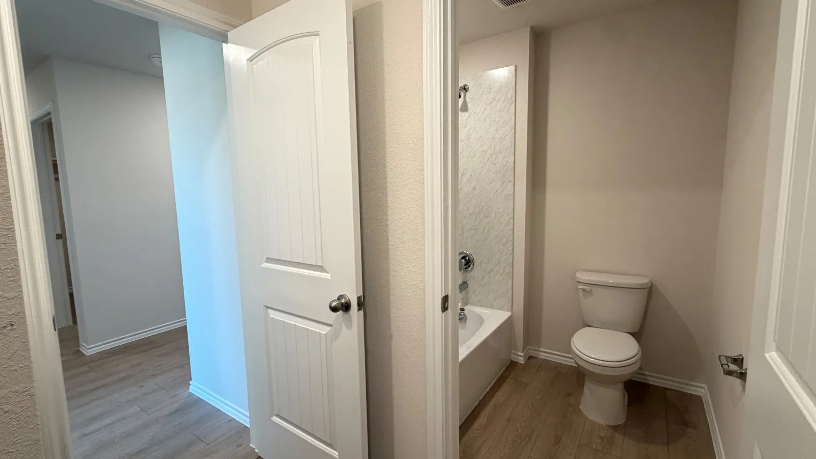 Full bathroom featuring a white tub/shower combination with a textured wall surround, a white toilet, and wood-finish flooring