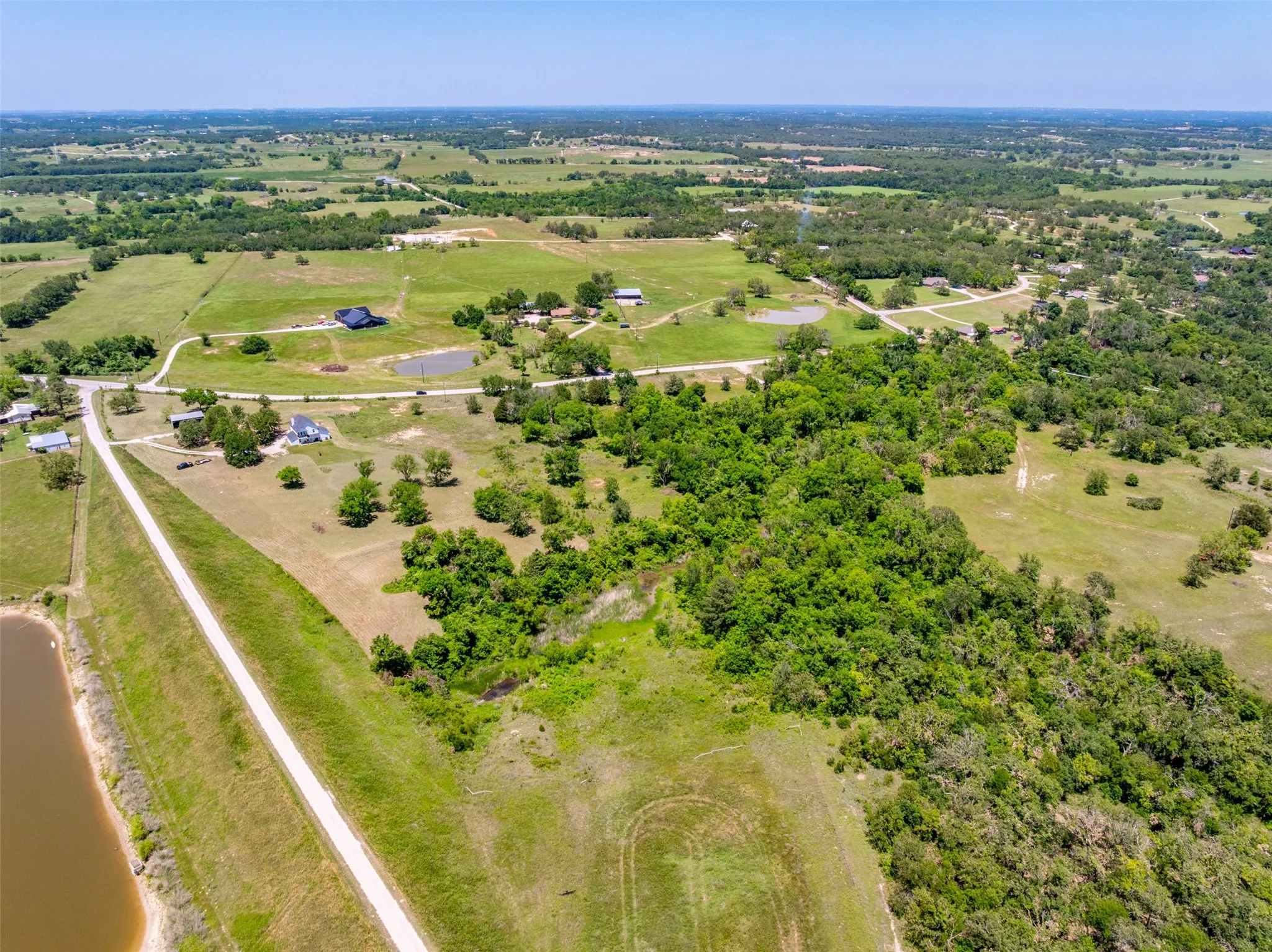 Expansive rural landscape featuring scattered homes, bodies of water, open fields, and wooded areas