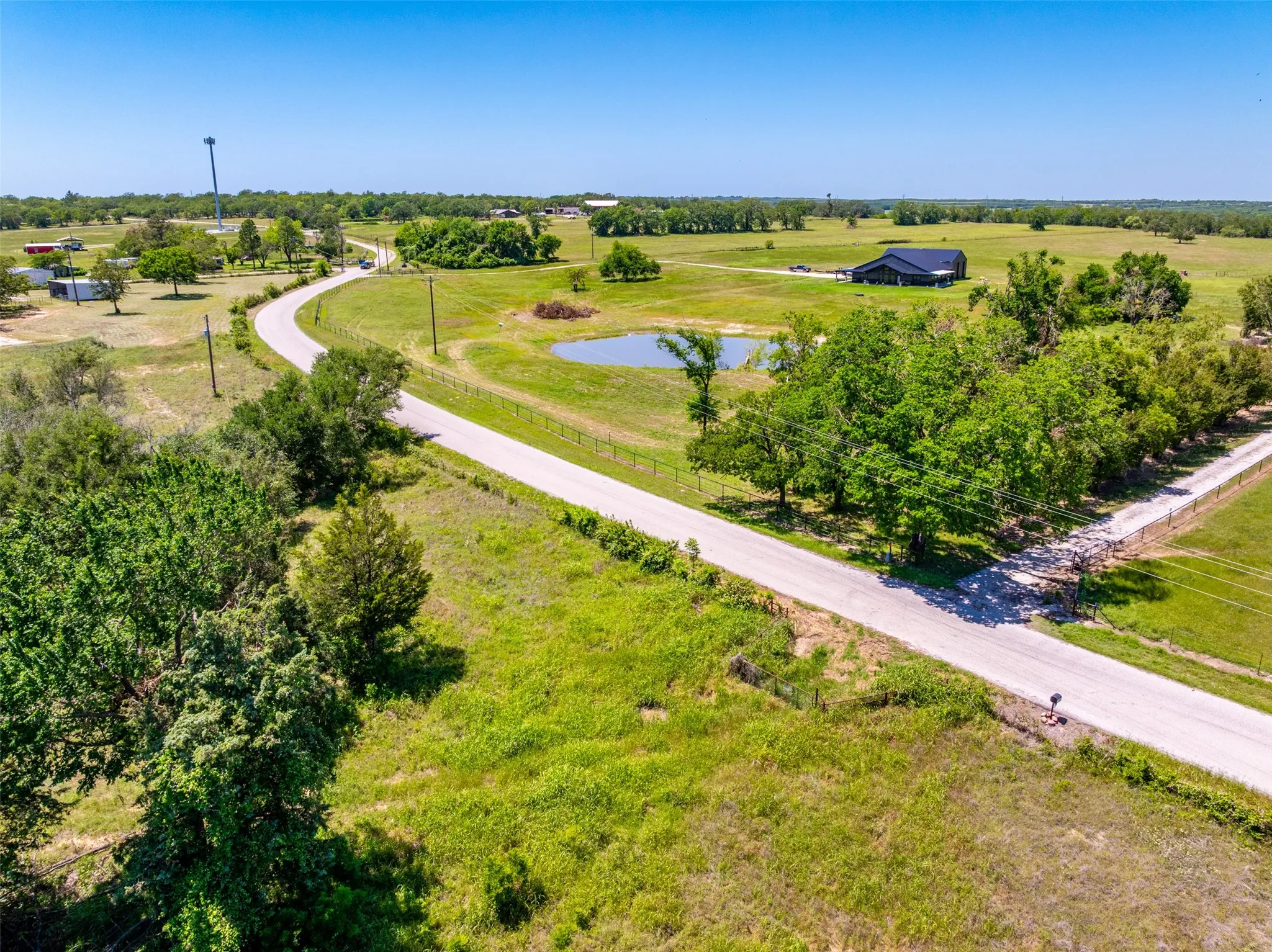 Expansive rural property featuring a winding paved road, a tranquil pond, and mature trees