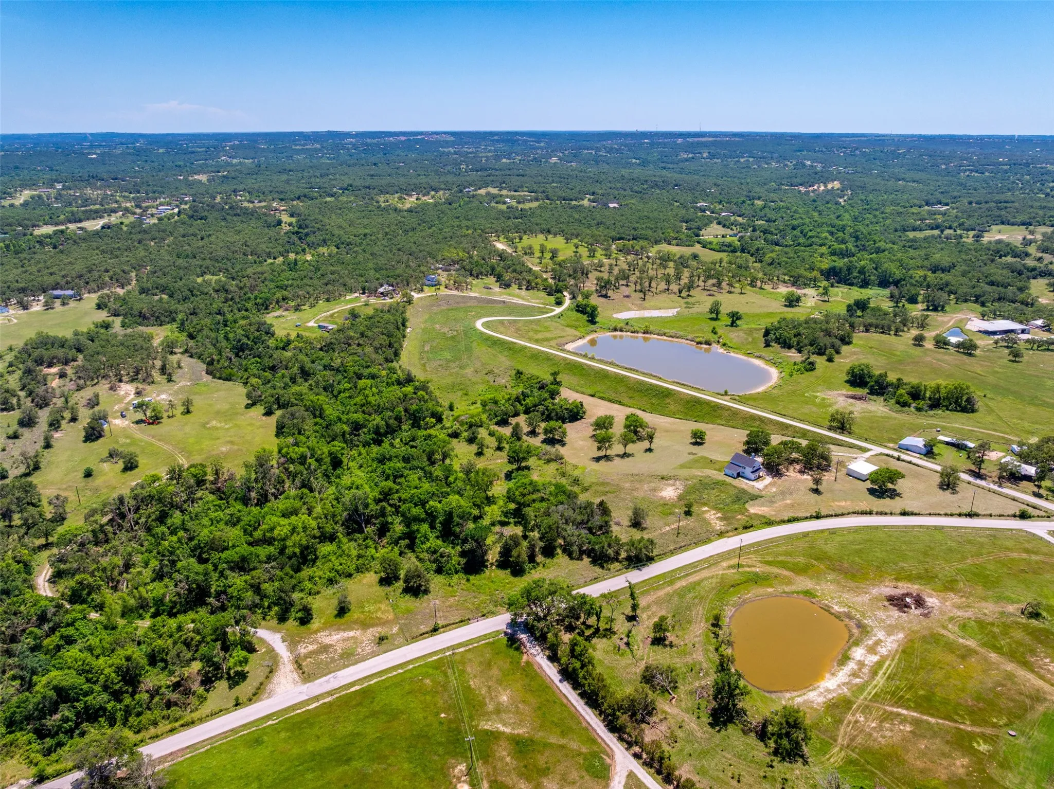 Expansive rural landscape featuring a mix of mature trees, open grassy areas, and two distinct ponds