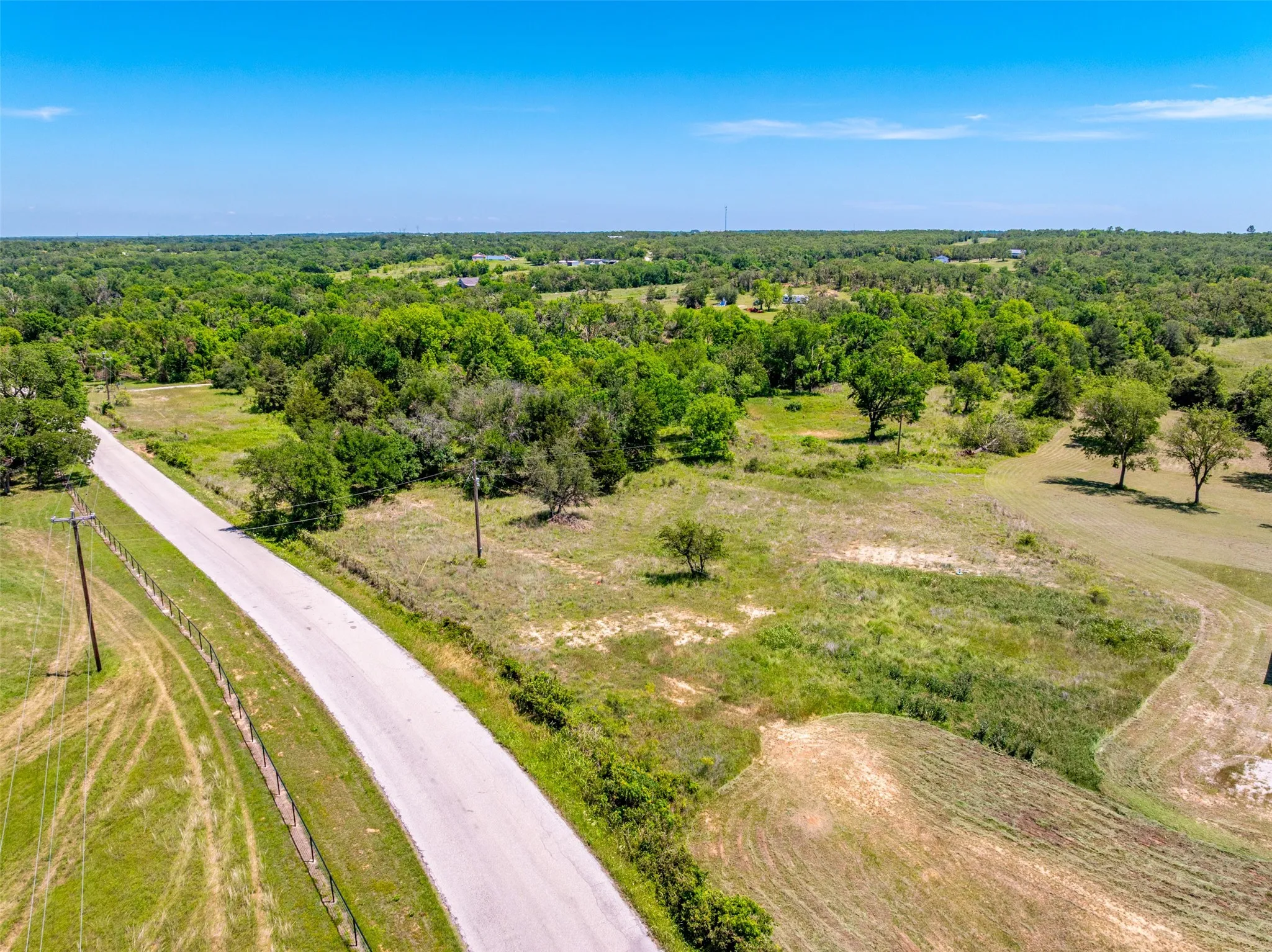 Rural landscape featuring a paved road, expansive green spaces, mature trees, and a clear blue sky
