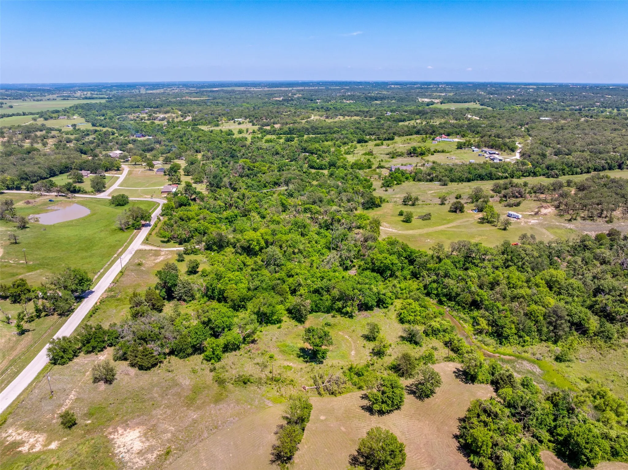 Expansive rural landscape featuring a mix of mature trees, open grassy areas, and a visible roadway