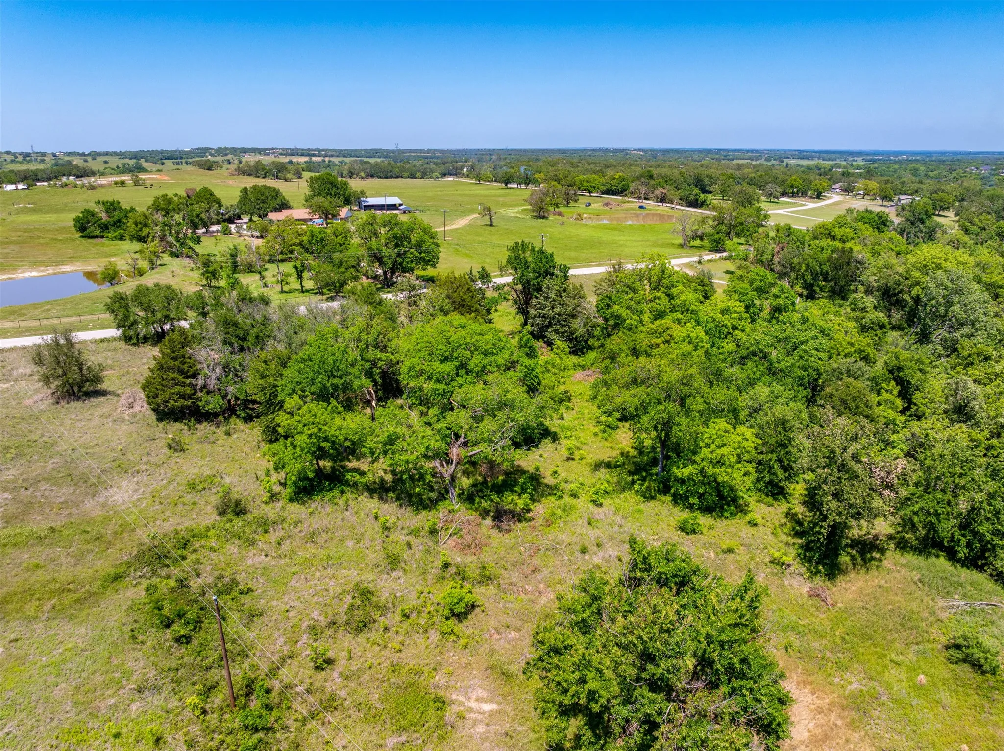 Expansive rural landscape featuring a prominent body of water, lush green fields, scattered mature trees, and a distant residence with outbuildings