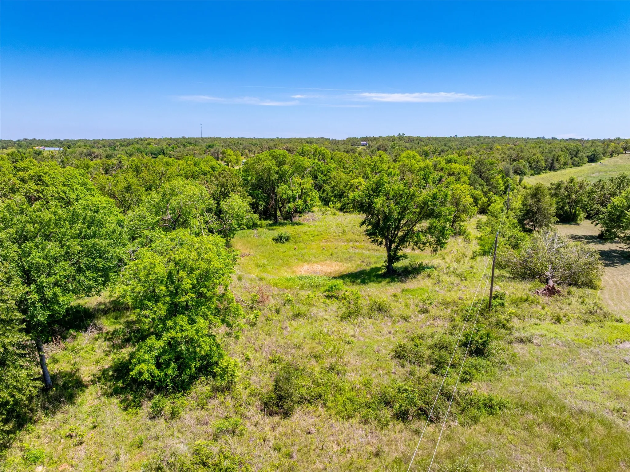 Expansive land featuring a clearing amidst dense tree lines, abundant natural foliage, and open grassland