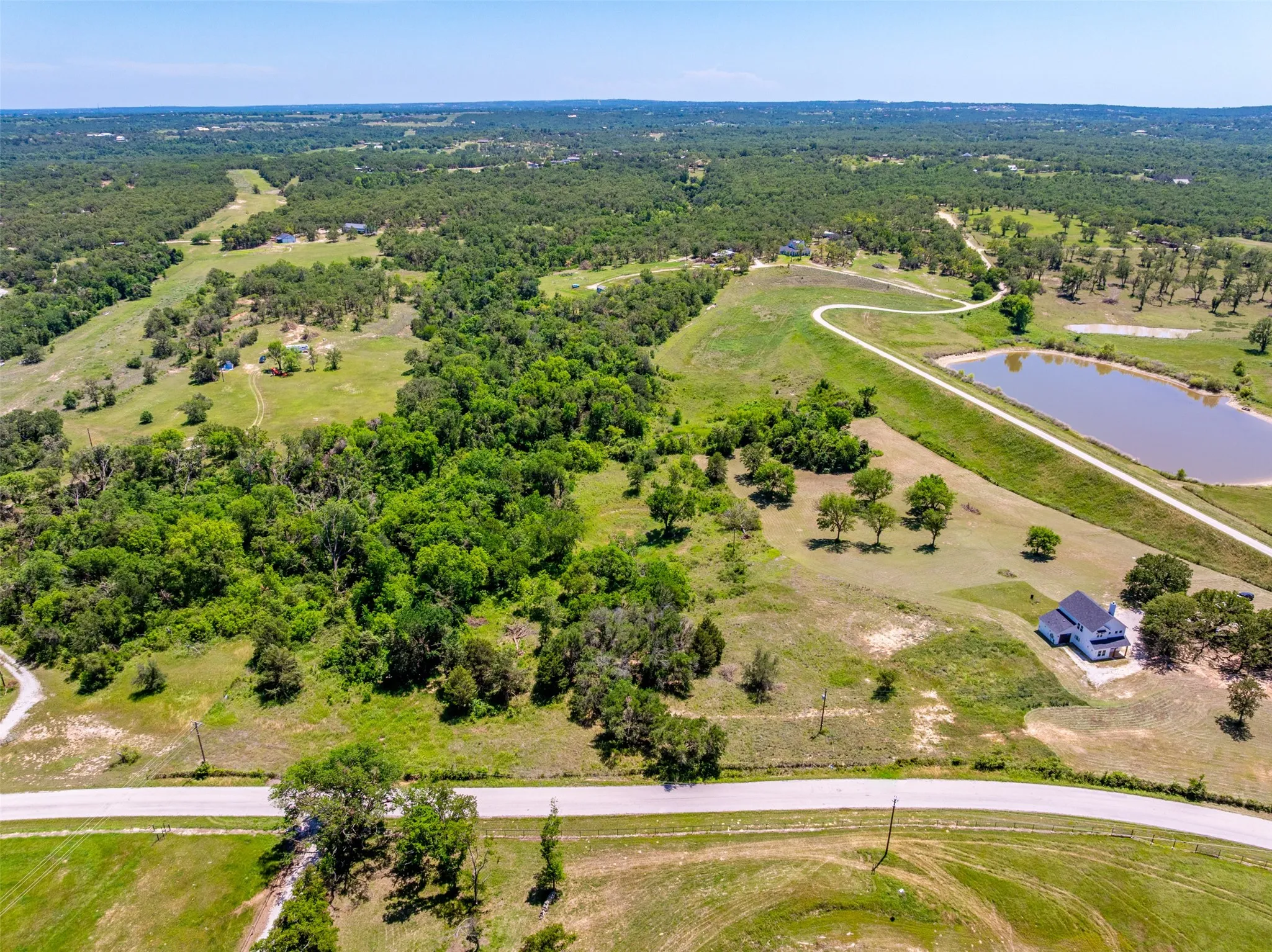 Expansive rural acreage featuring a large pond, mature trees, open grassy areas, and a paved road frontage