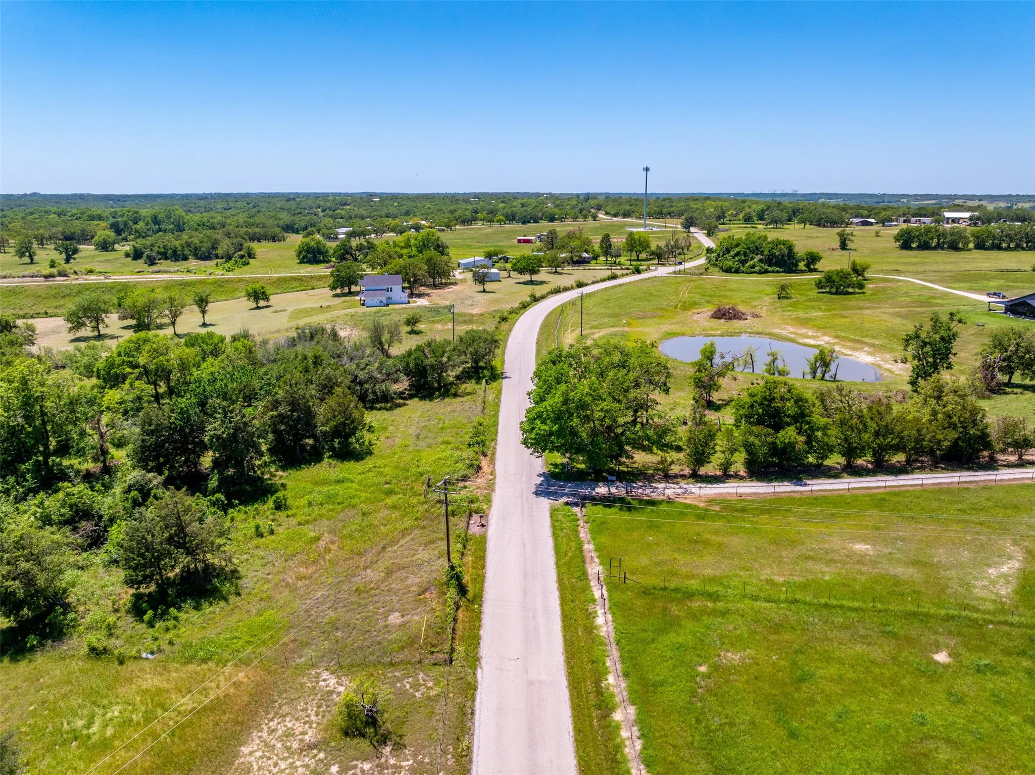 Expansive rural landscape featuring a winding paved road, scattered mature trees, and open green fields