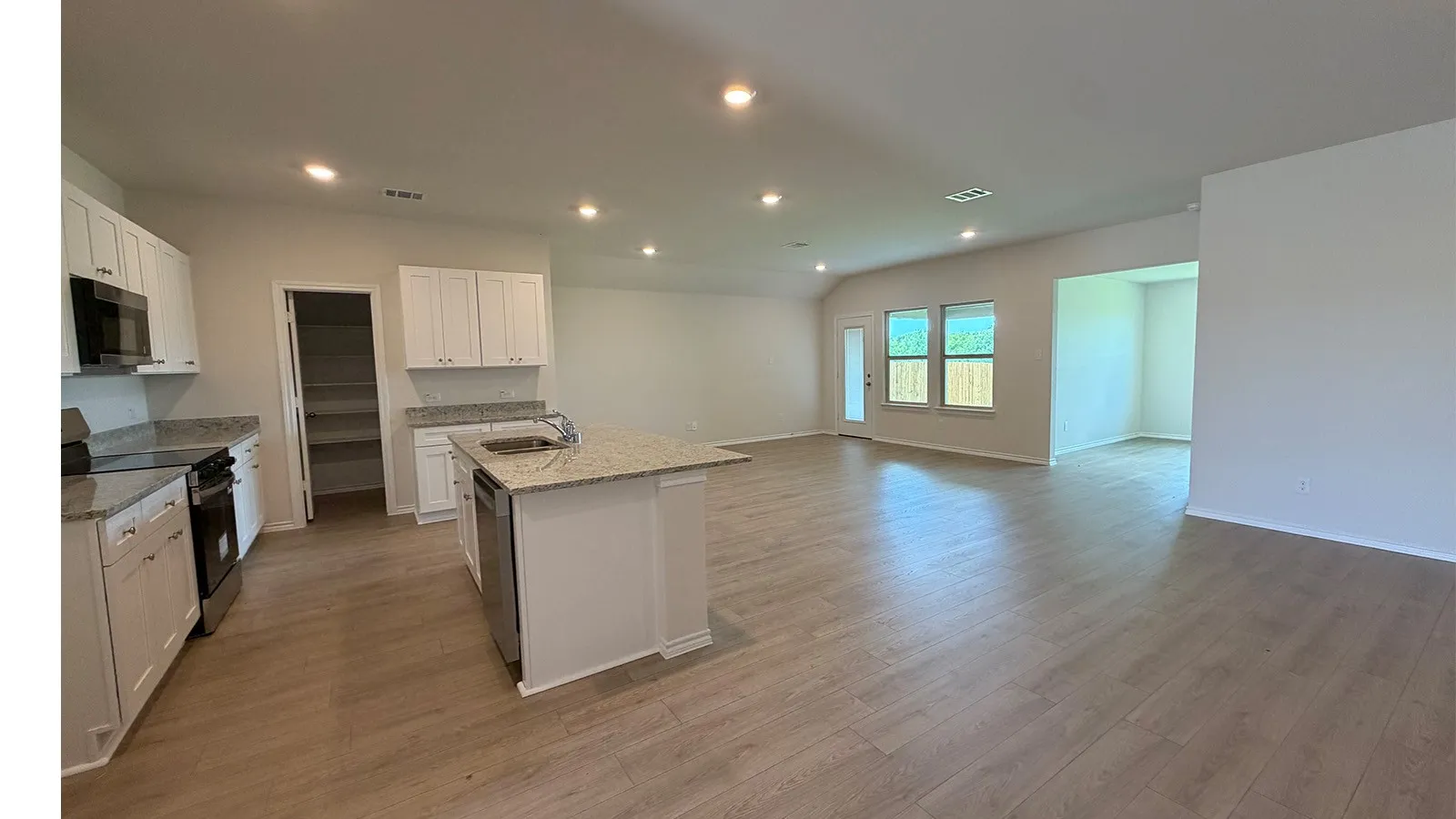 Open-concept living area featuring wood-finish flooring, recessed lighting, and a kitchen with white cabinetry