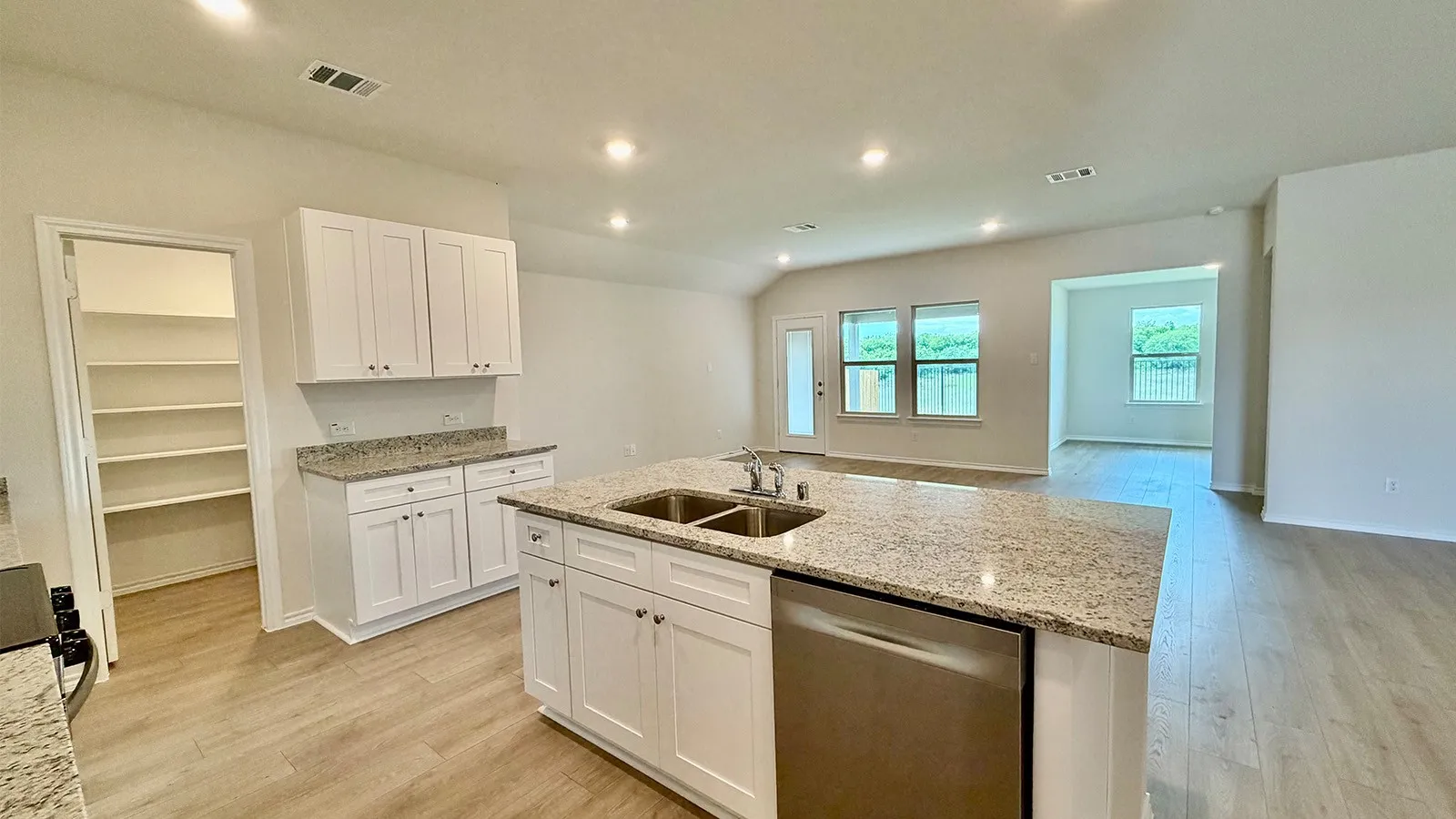 Modern kitchen featuring an expansive center island with an undermount dual sink, white cabinetry, granite-finish countertops, and wood-finish flooring