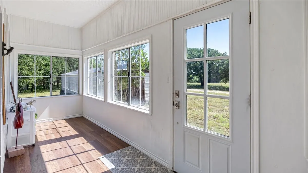 Sunroom featuring multiple windows, a paneled entry door with glass inserts, wood-finish flooring, and white beadboard walls