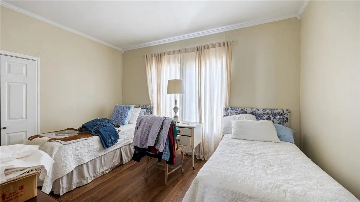 Room featuring wood-finish flooring, neutral wall tones, crown molding, and a white paneled door