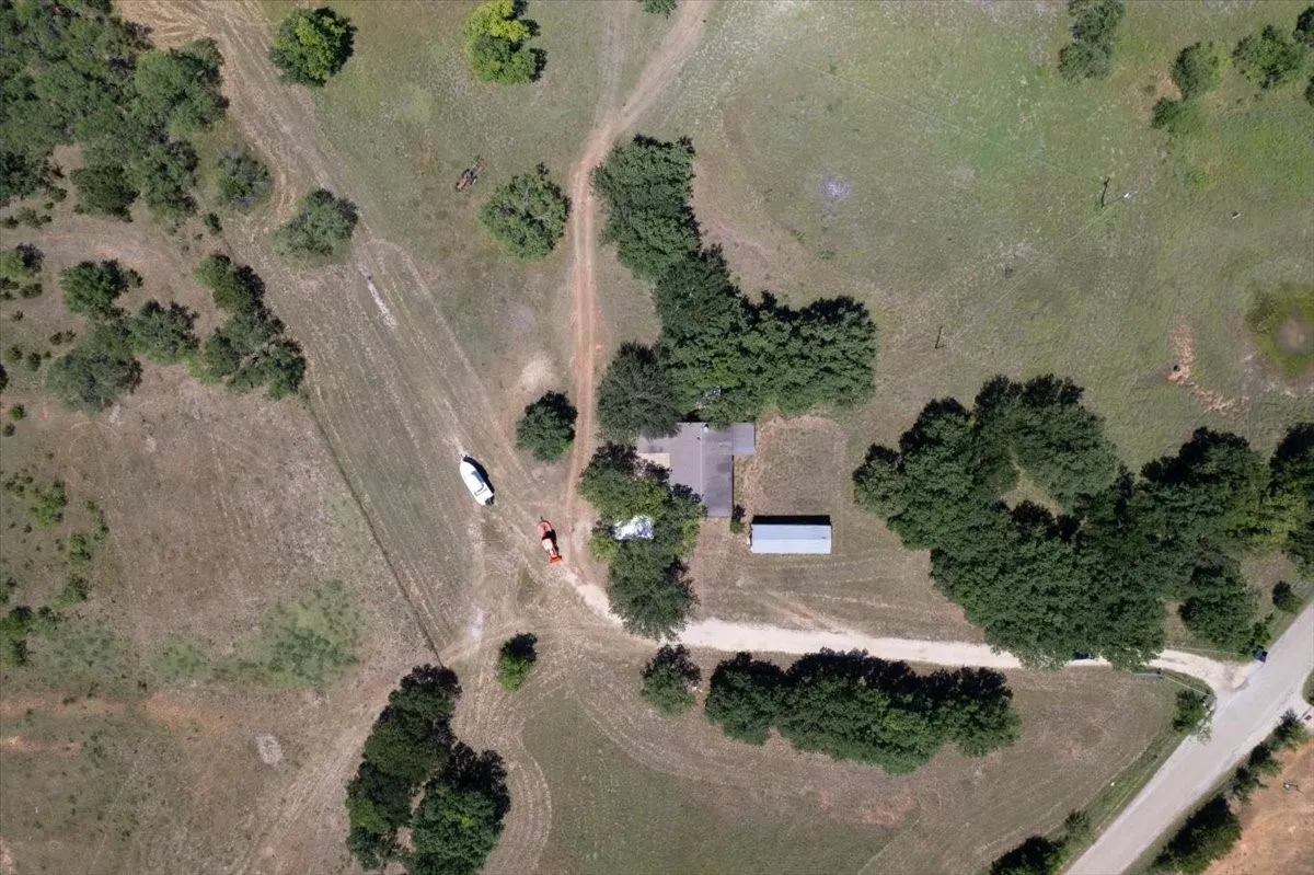 Expansive parcel featuring a central residence, a separate outbuilding with a metal roof, mature trees, open grassland, and multiple unpaved access paths