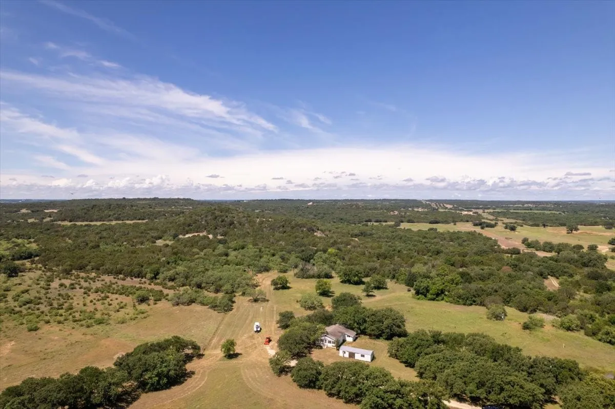Expansive rural landscape featuring a main dwelling with an additional structure, surrounded by mature trees and open fields