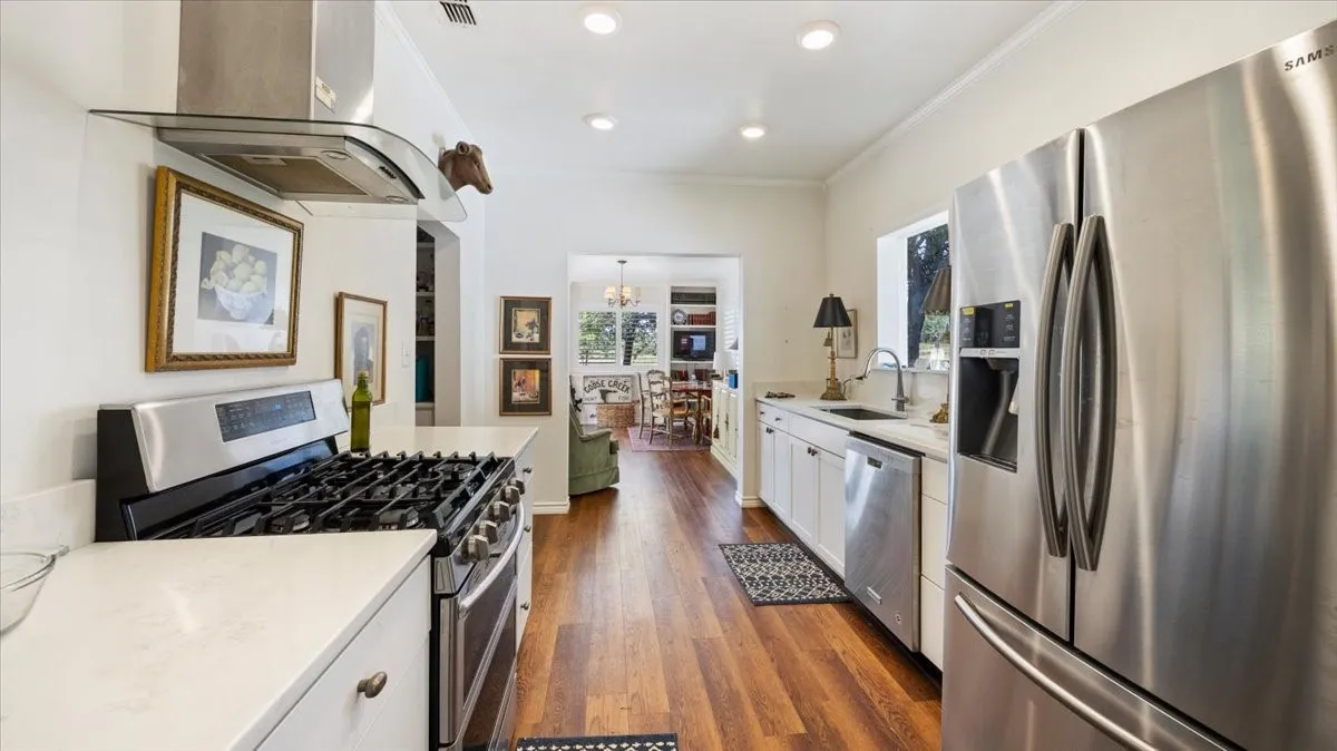 Kitchen featuring stainless steel appliances, white cabinetry, solid surface countertops, a gas range with an overhead vent hood, and wood-finish flooring