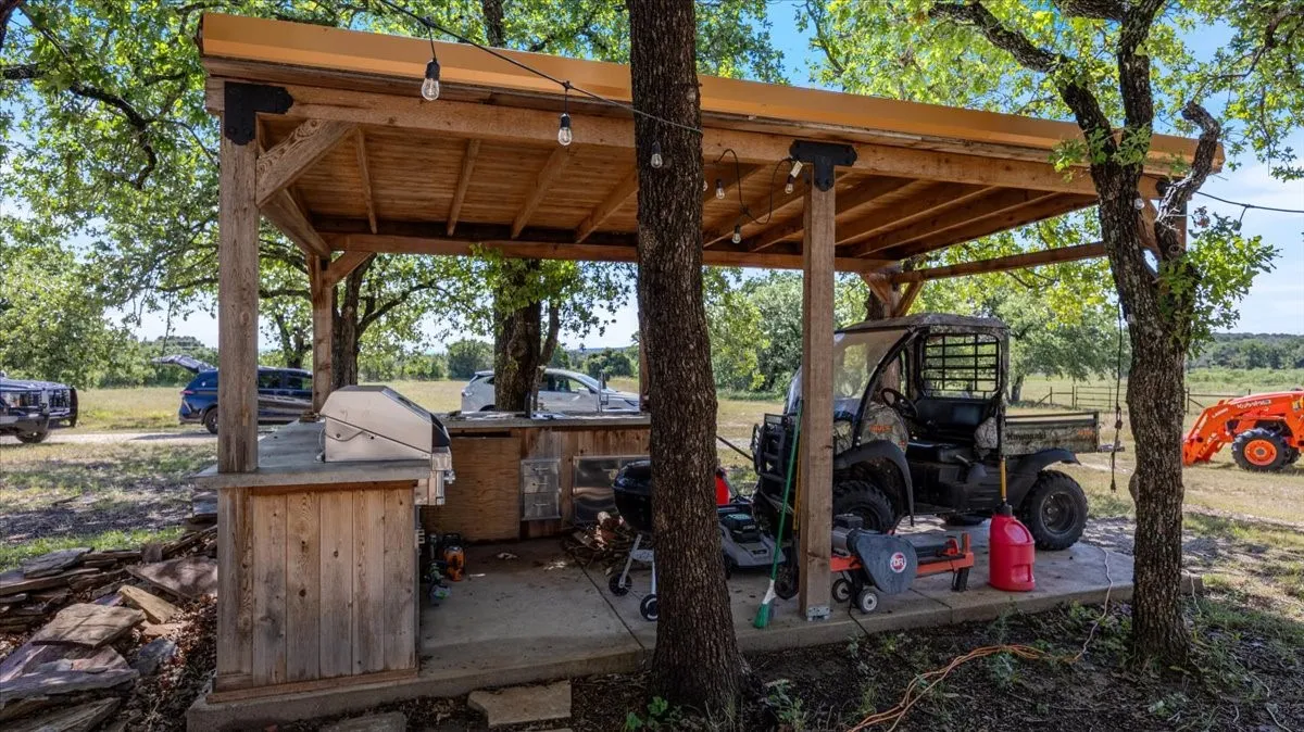 Outdoor entertainment area featuring a pergola with string lighting, a built-in grill station with a stone-finish countertop, and a concrete pad