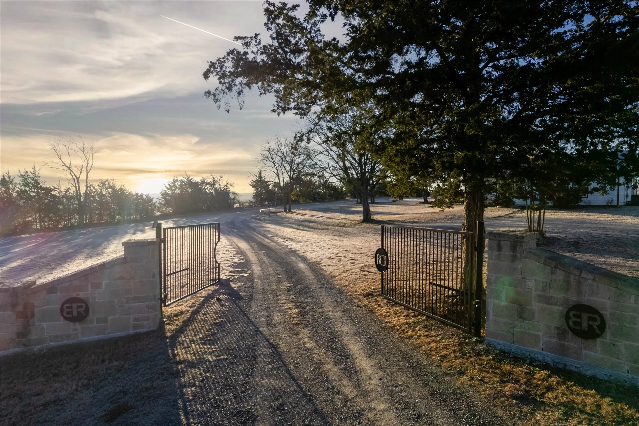 Gated property entrance with stone pillars, featuring a private gravel driveway and mature trees