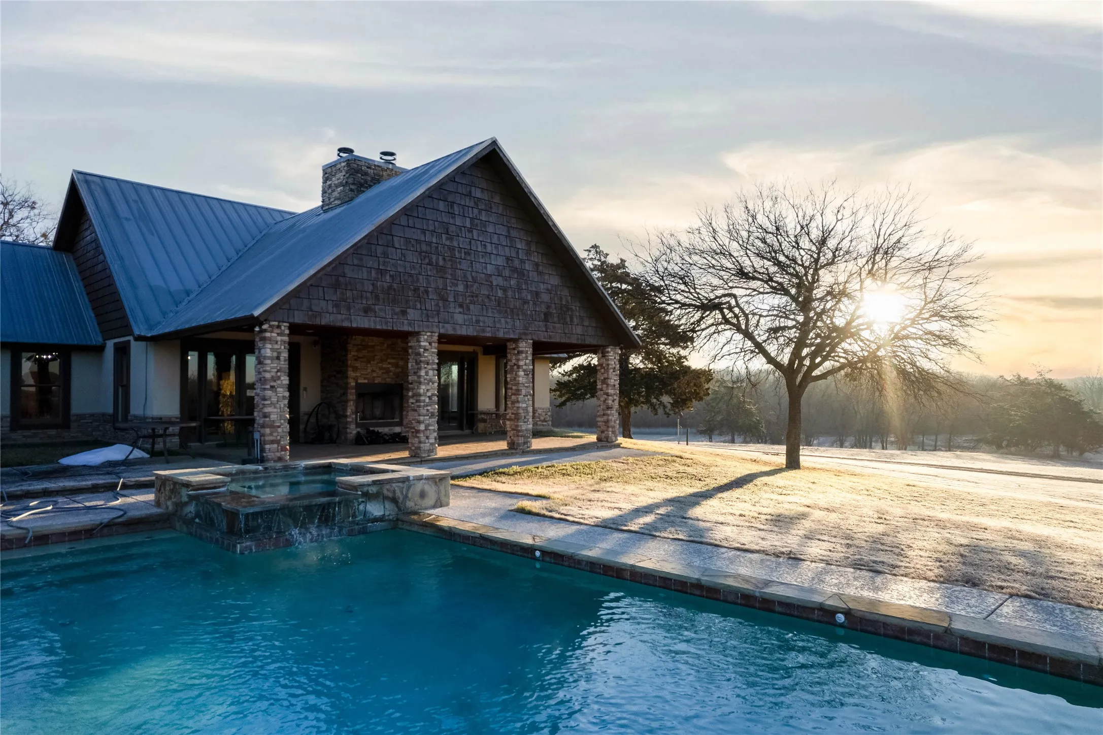 Exterior featuring a pitched metal roof, stone and wood-shake siding, and a covered patio with stone columns
