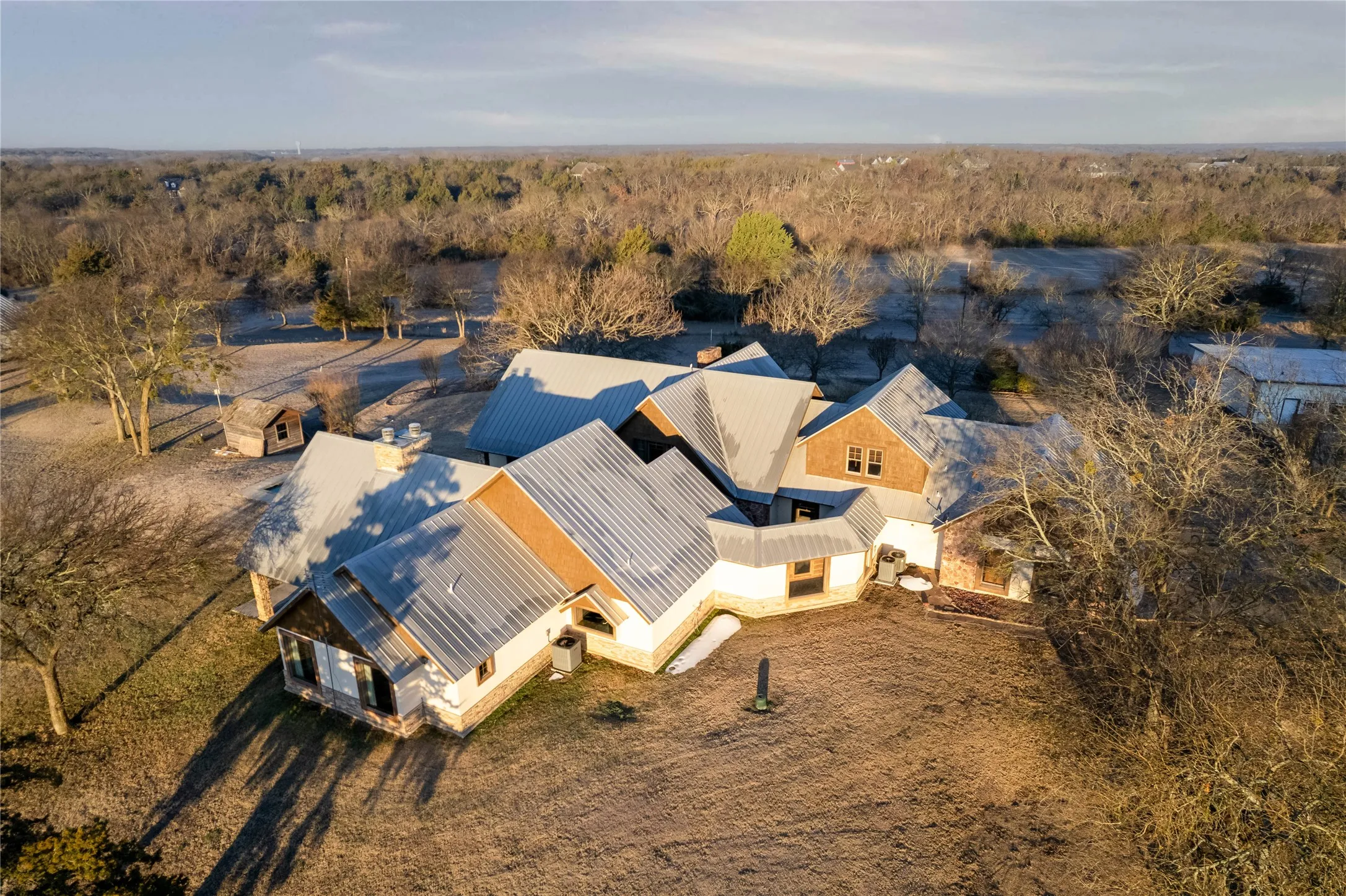 Expansive property featuring a multi-gabled metal roofline, a blend of stone and wood-look siding, and a surrounding natural landscape
