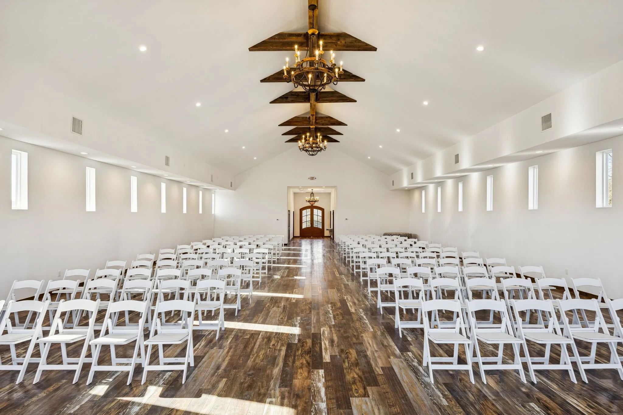Spacious hall featuring a vaulted ceiling with exposed wood beams, recessed lighting, and multiple vertical windows