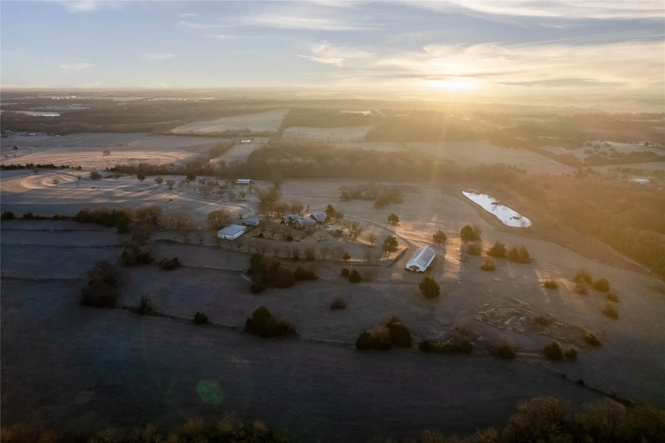 Expansive rural landscape featuring multiple structures, cultivated fields, and natural water features