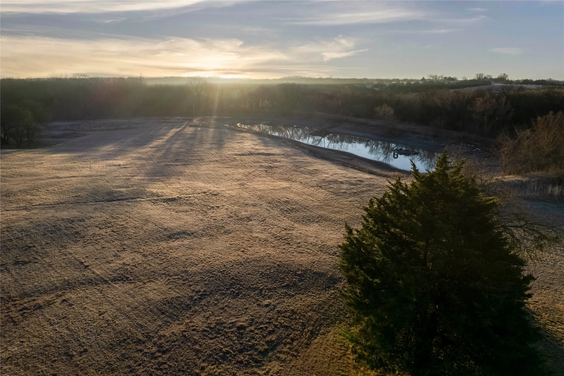 Expansive land parcel featuring a natural pond, scattered trees, and undulating terrain