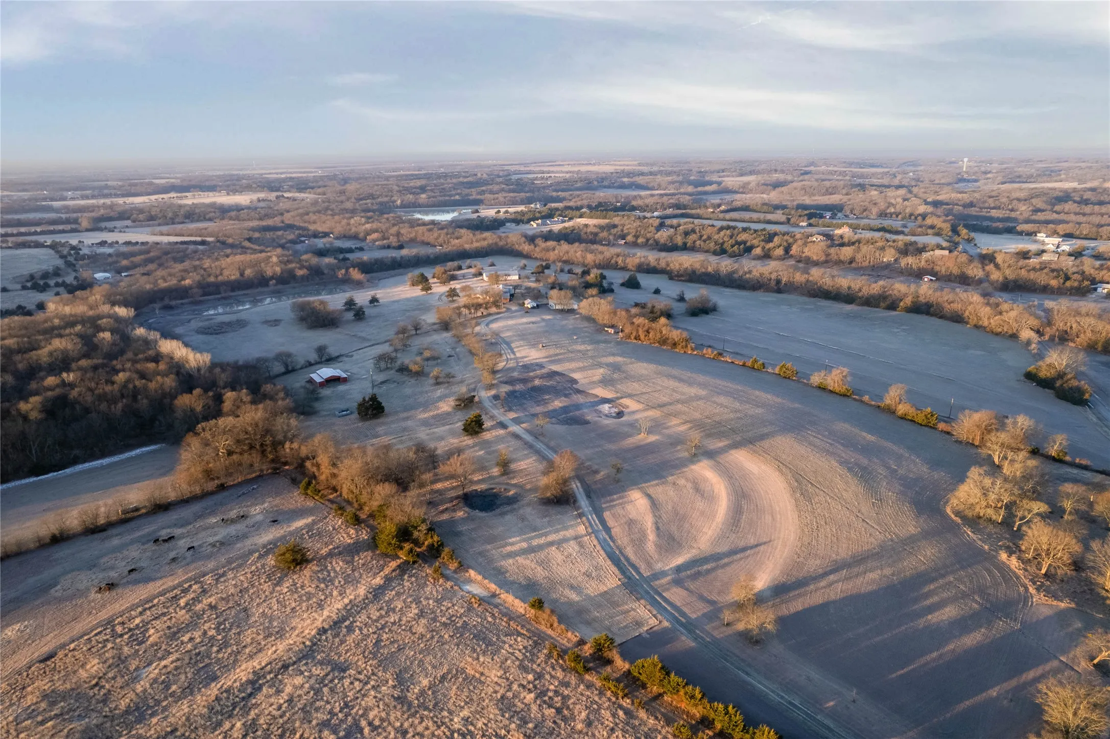 Expansive rural landscape featuring open fields, scattered mature trees, and natural bodies of water