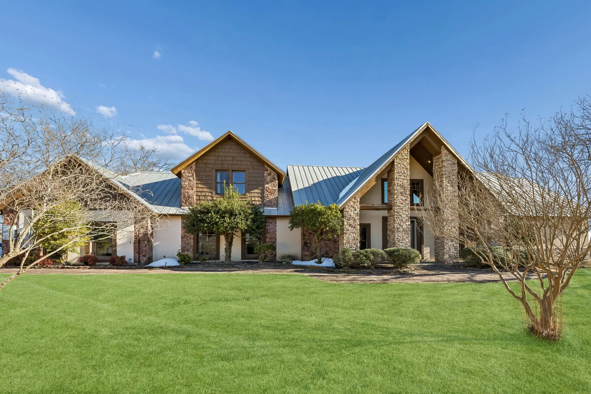 Exterior featuring stone and stucco finishes, a prominent metal roof, and multiple gables
