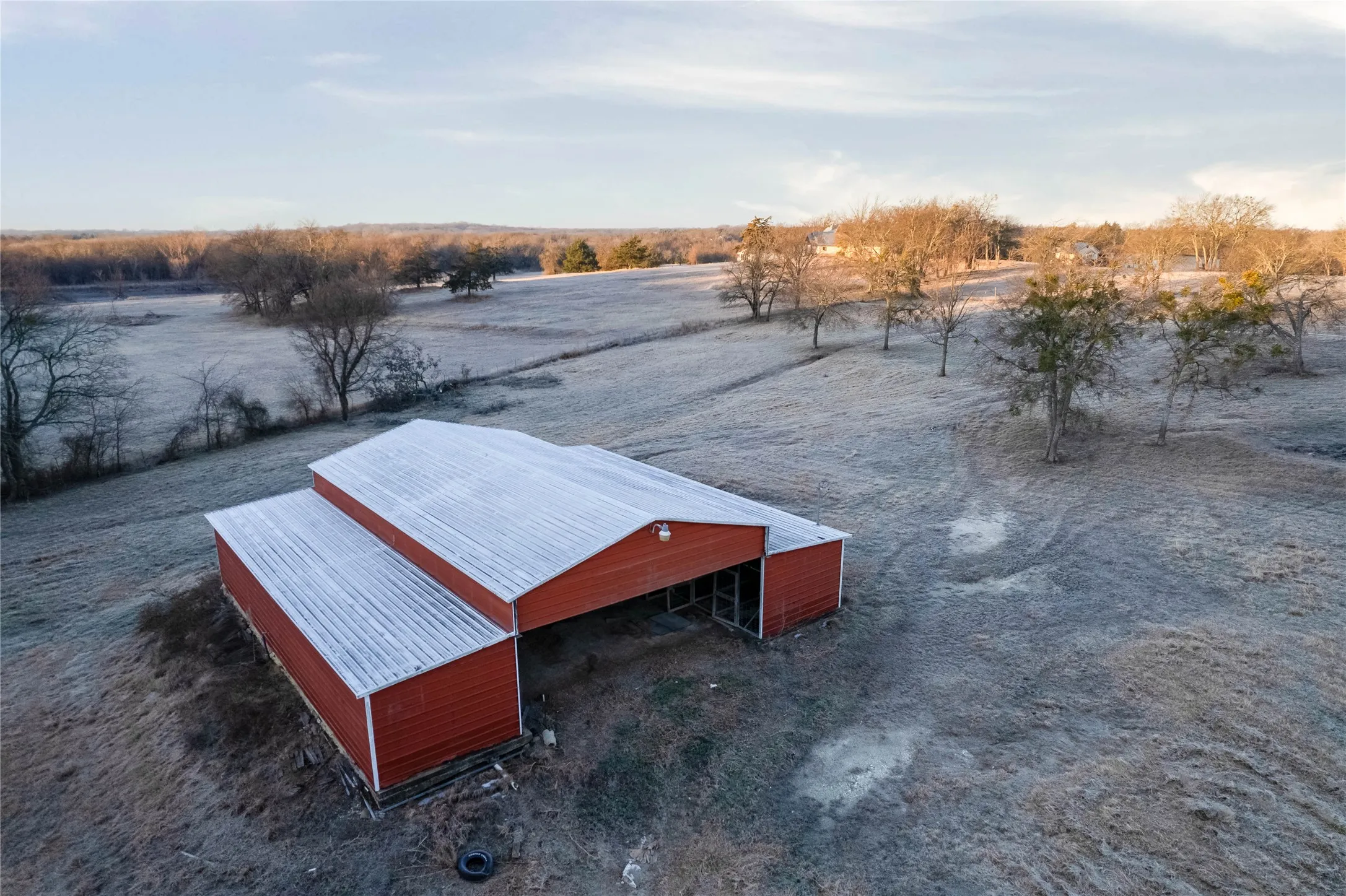 Red barn structure with a silver corrugated metal roof, surrounded by expansive, undeveloped land