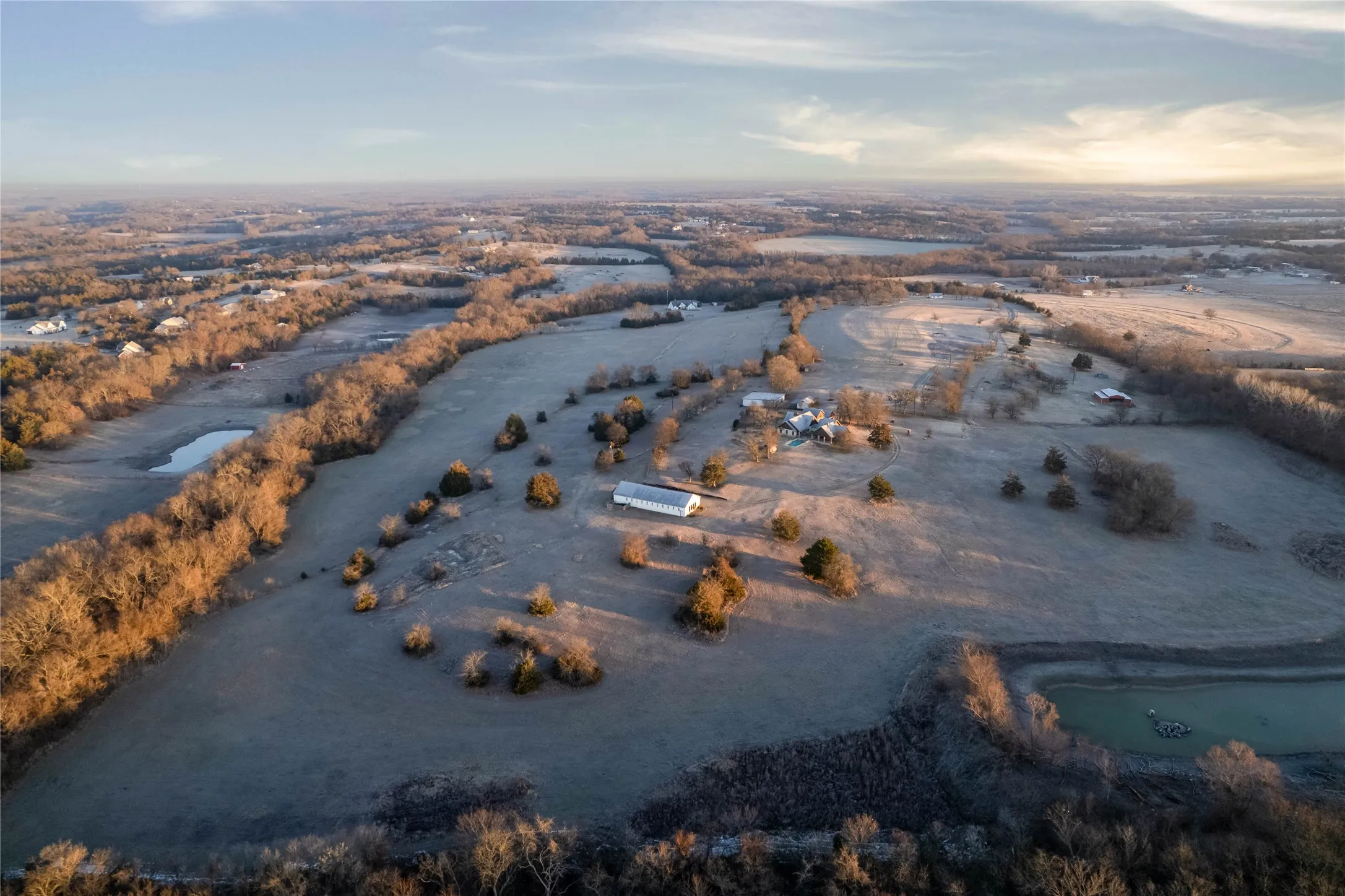 Expansive property featuring rolling terrain, multiple outbuildings, and mature trees