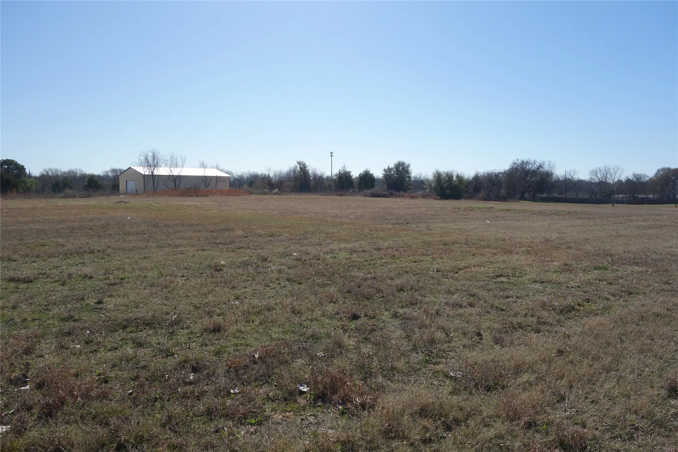 Expansive open land featuring a clear sky overhead and a distant structure with a light-colored roof