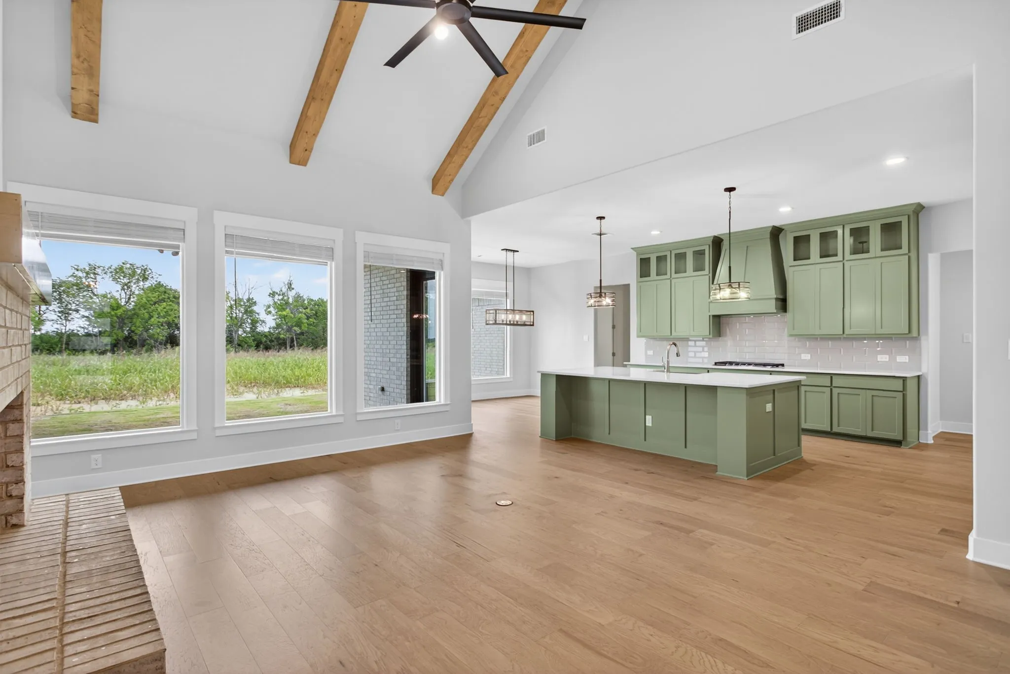 Open-concept living space featuring wood-finish flooring, a vaulted ceiling with exposed beams and a ceiling fan, and a brick-finish fireplace