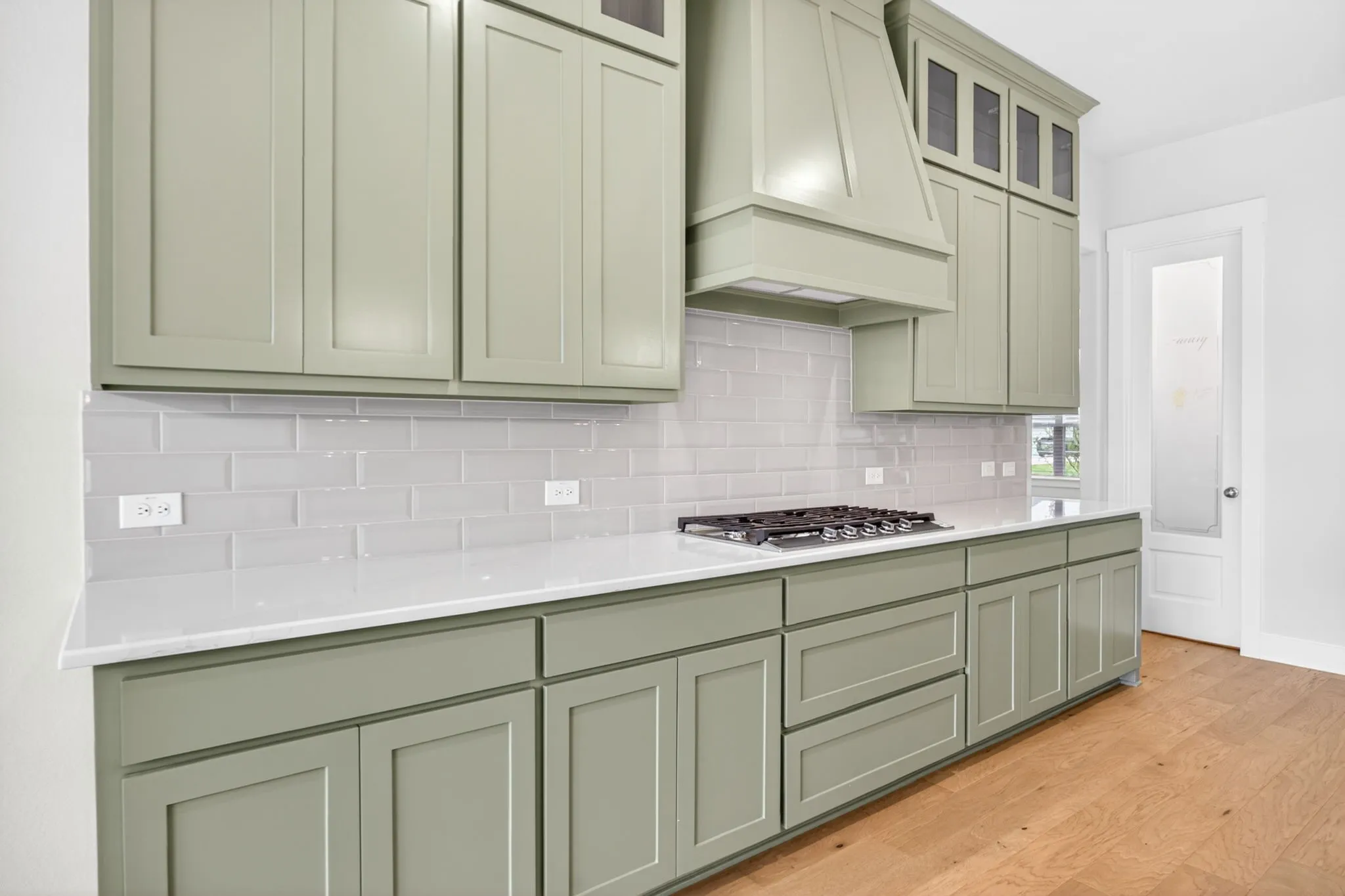Kitchen featuring green shaker cabinetry, white countertops, a gas range with a matching range hood, a subway tile backsplash, and wood-finish flooring