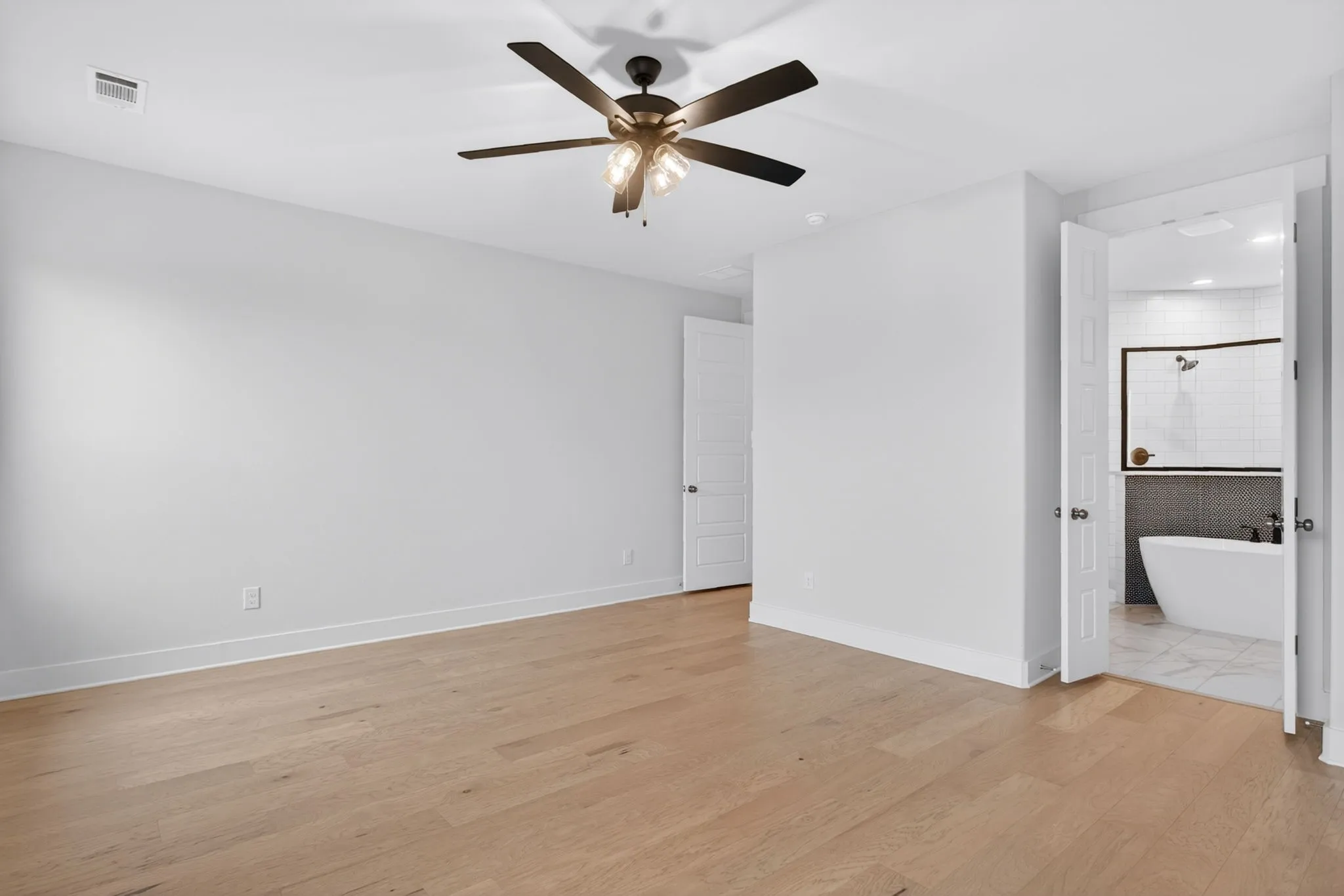 Spacious room featuring wood-finish flooring, a contemporary ceiling fan, and crisp white walls