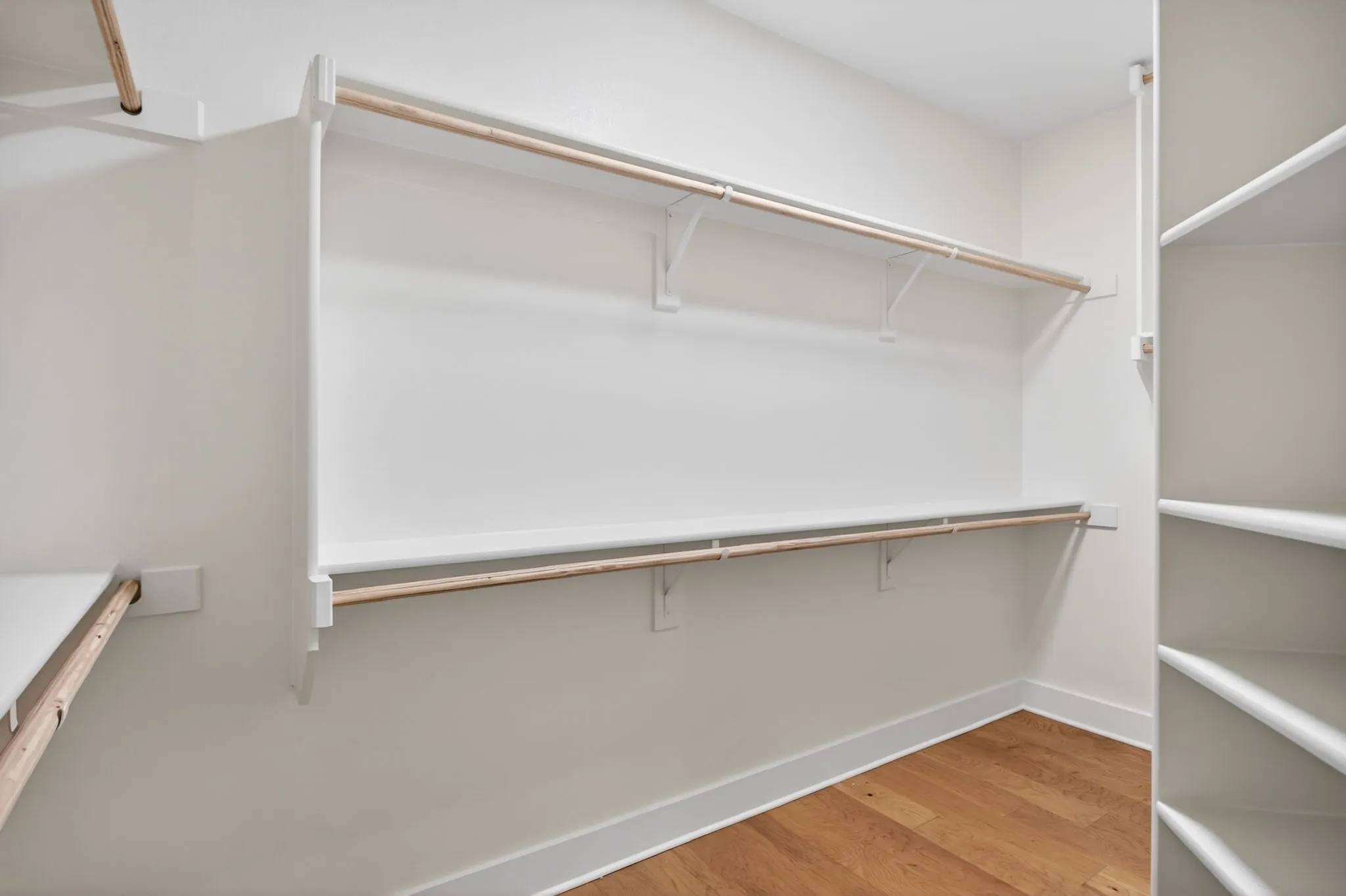 Walk-in closet featuring wood-finish flooring, white built-in shelving, white walls, and white baseboards