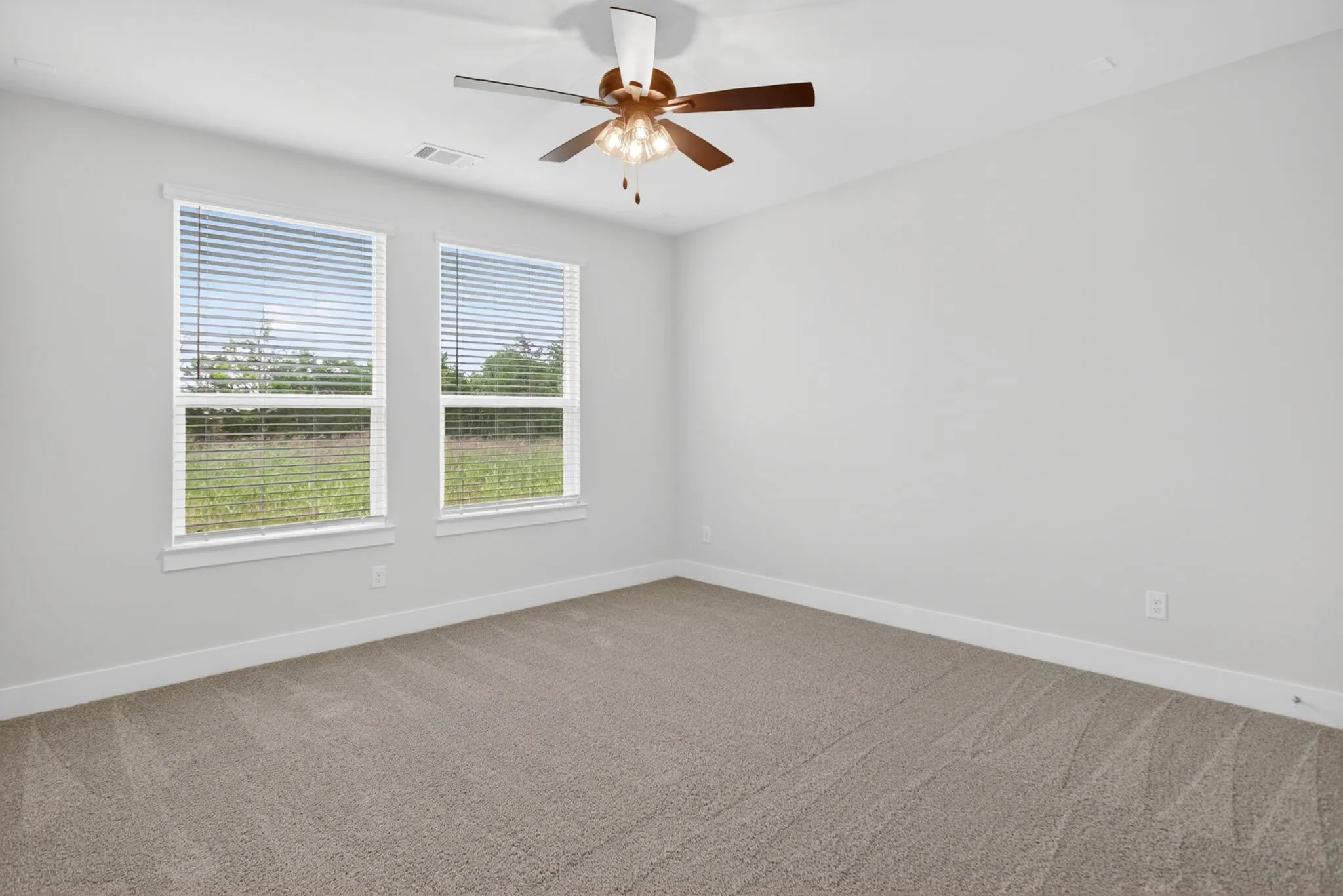 Carpeted room featuring two large windows with blinds, a ceiling fan with integrated lighting, and neutral wall tones