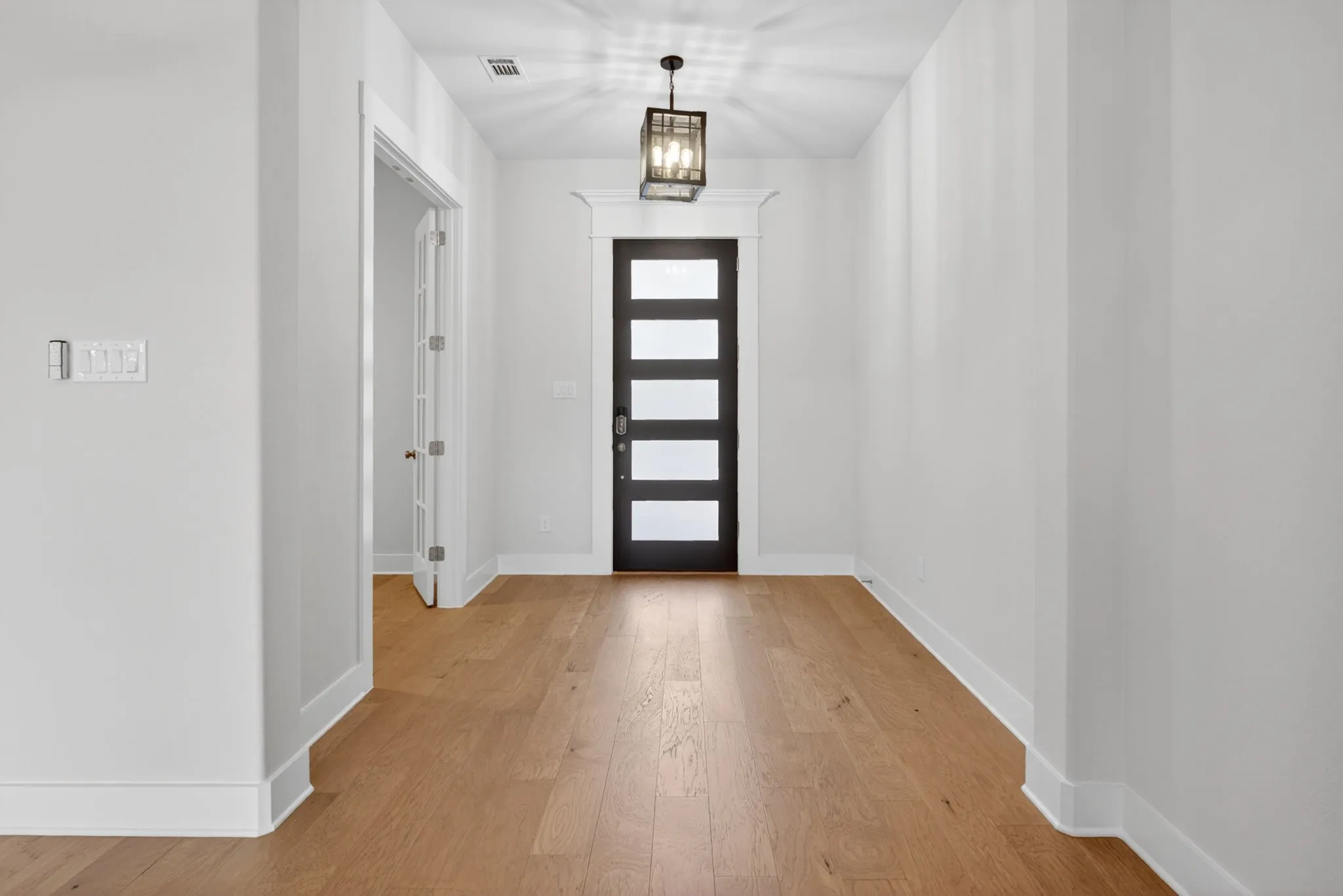 Spacious entryway featuring wood-finish flooring, a contemporary pendant light fixture, and a modern door with frosted glass panels