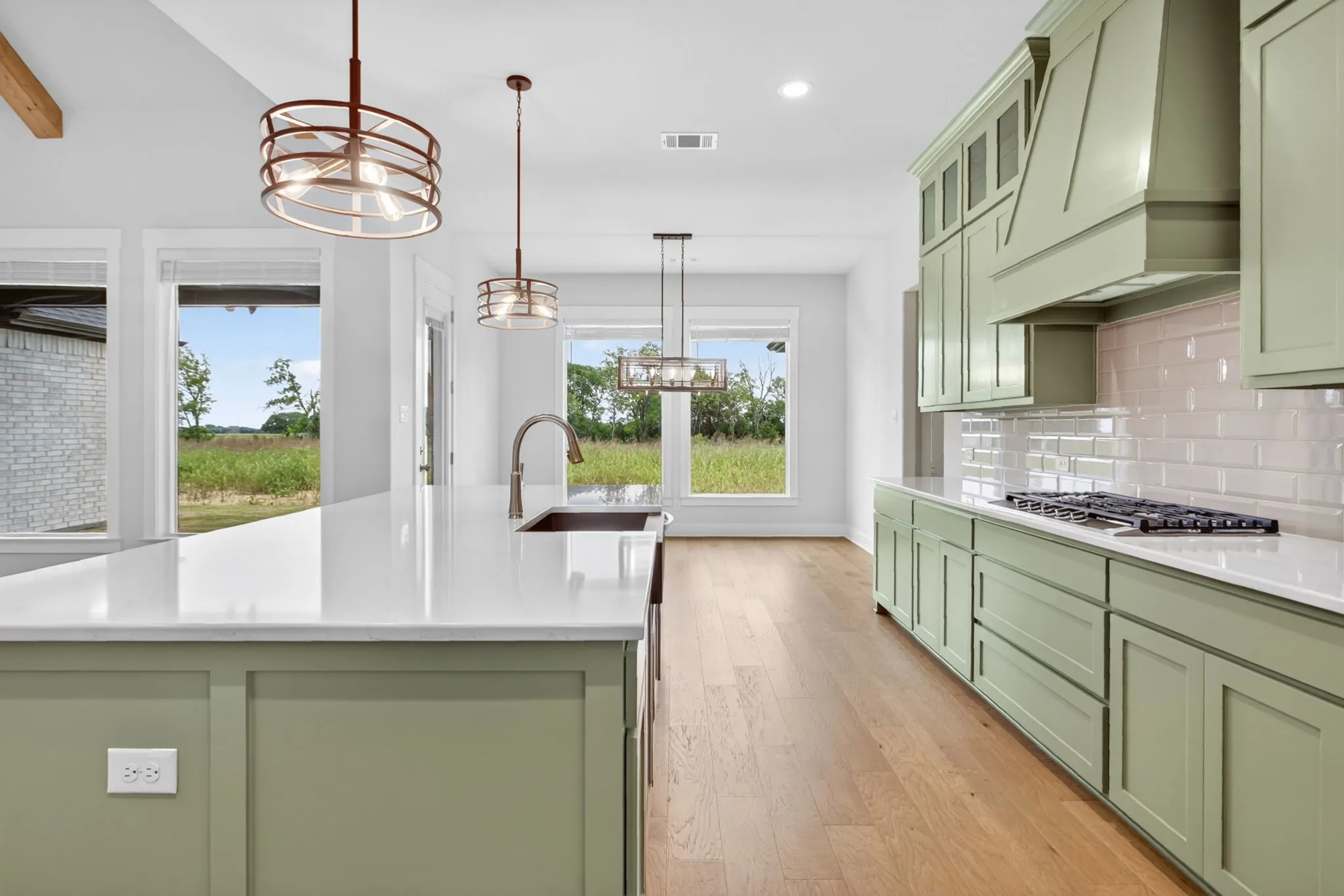Gourmet kitchen featuring sage green shaker cabinetry, quartz countertops, a gas range with a custom range hood, and a large island with an undermount sink