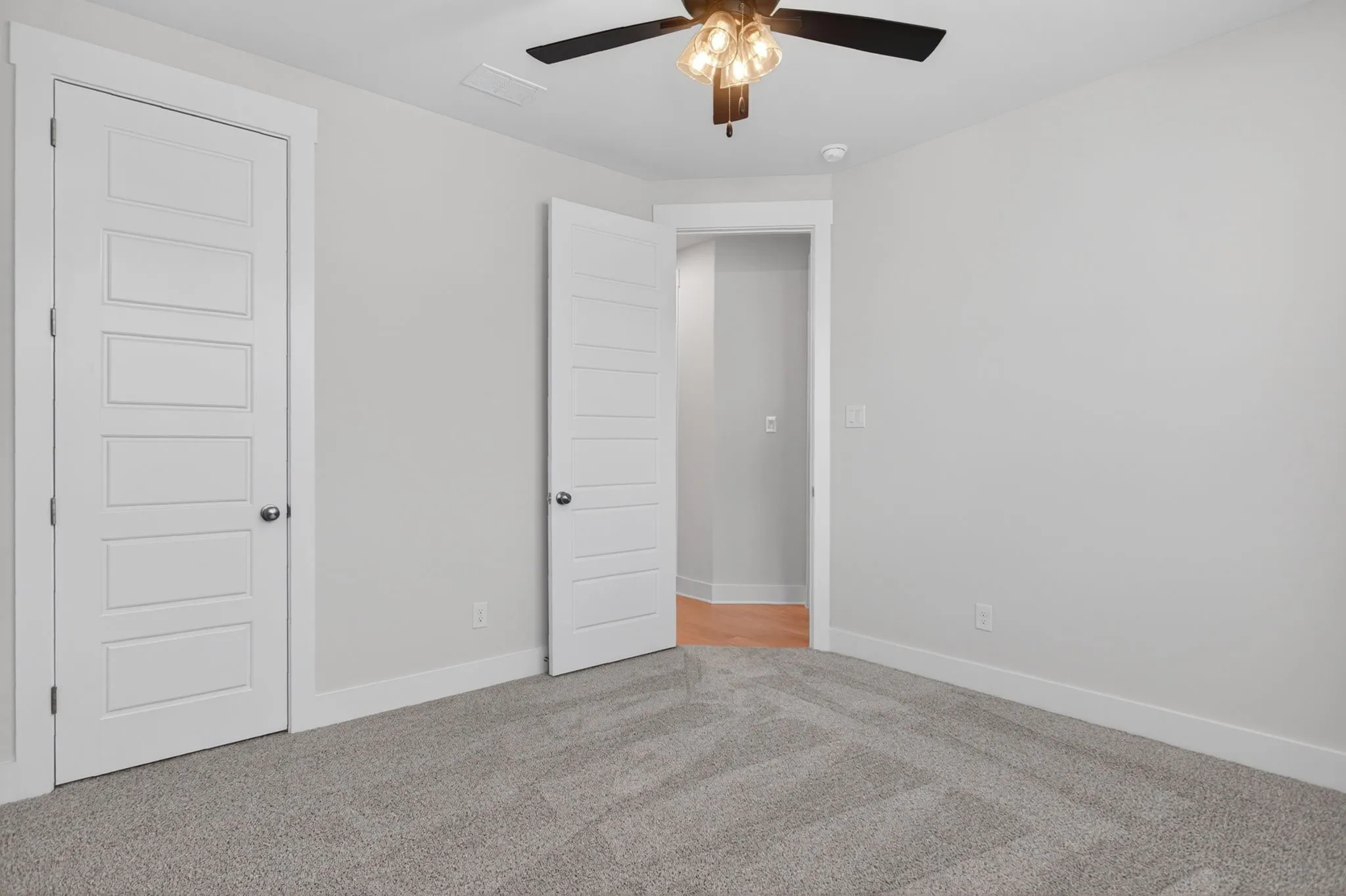 Neutral-toned room featuring a ceiling fan with integrated lighting, soft gray carpeting, and white baseboards