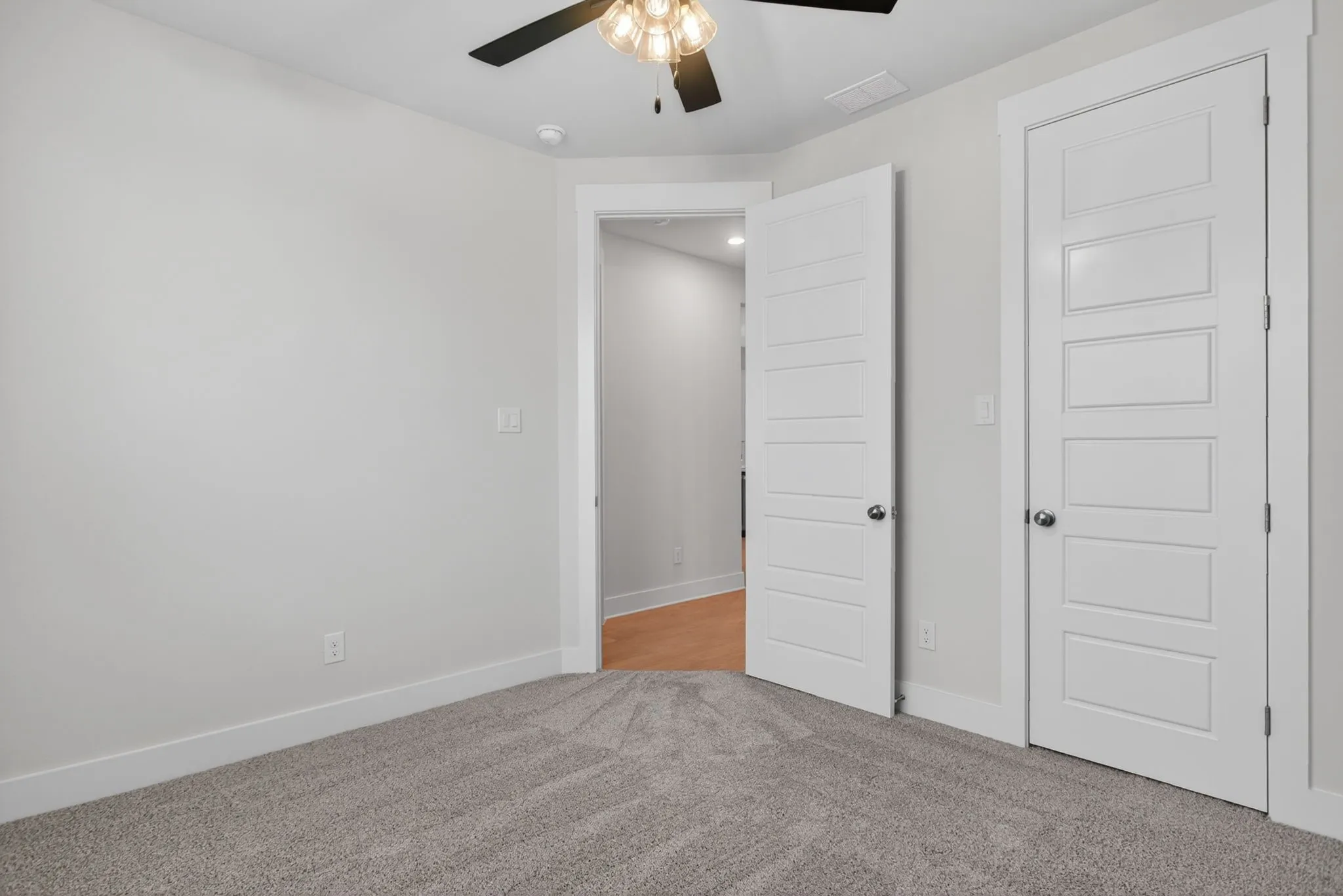 Neutral tone walls with white trim, gray textured carpeting, and a ceiling fan with integrated lighting
