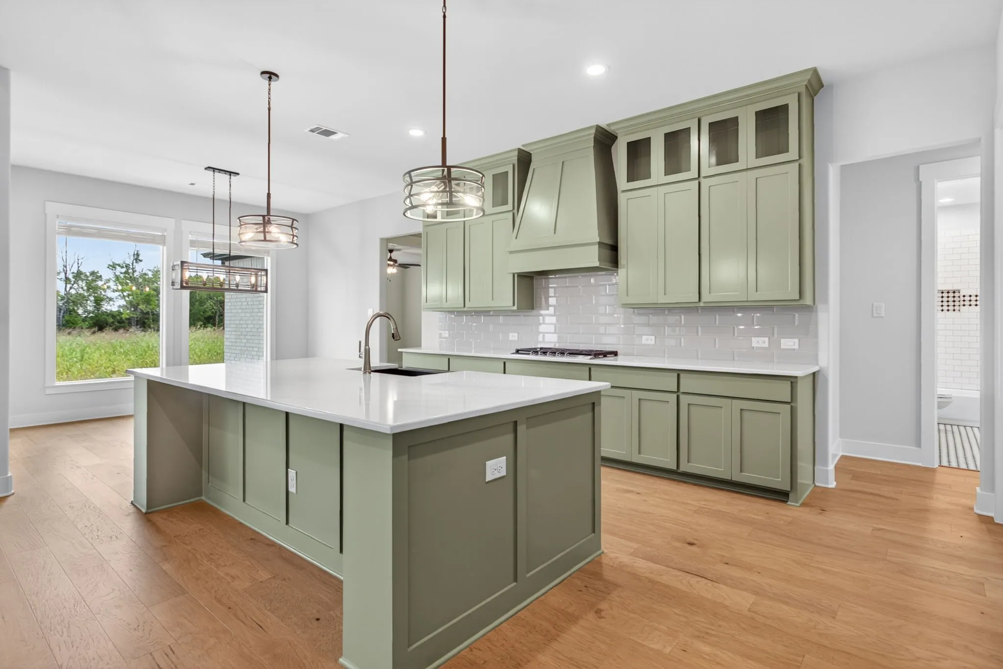 Spacious kitchen featuring a large island with a sink, light green cabinetry, white countertops, subway tile backsplash, and light wood-finish flooring