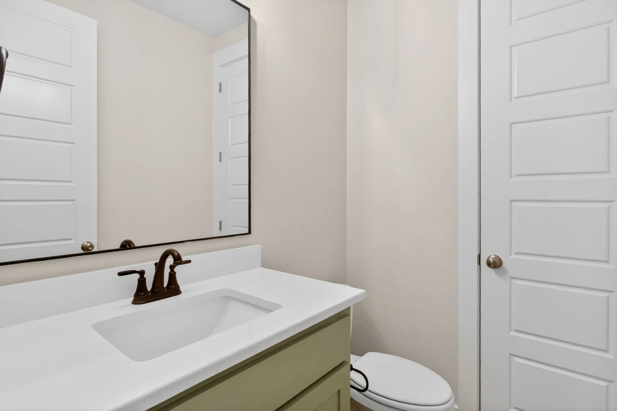 Bathroom featuring a white integrated sink, bronze-finish faucet, light green vanity cabinet, white countertop, and a framed mirror