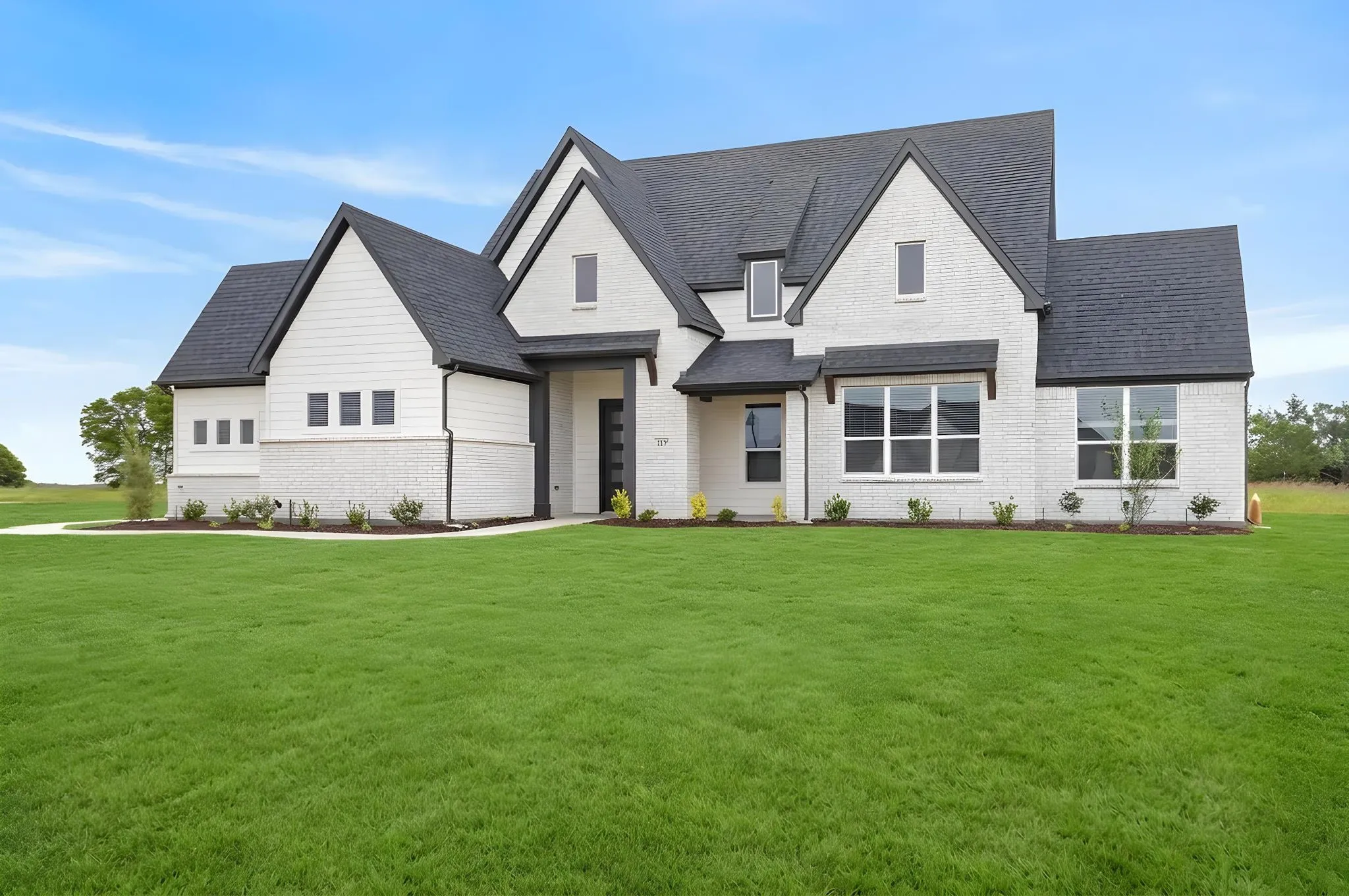 Modern farmhouse exterior featuring white brick and horizontal siding, dark shingle roof, dark trim accents, and a professionally landscaped front yard