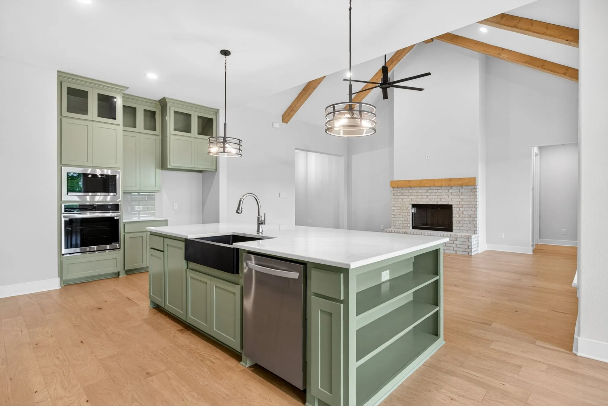 Modern kitchen featuring green cabinetry, stainless steel appliances, and a central island with a white countertop and black farmhouse sink