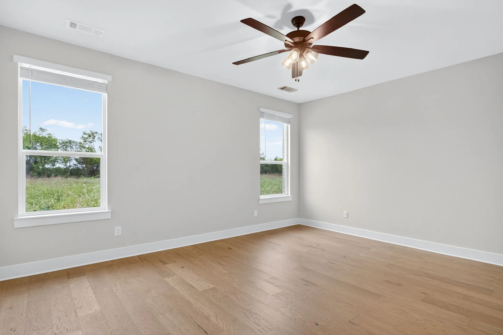 Spacious room featuring wood-finish flooring, light gray walls, white trim, and a ceiling fan with integrated lighting