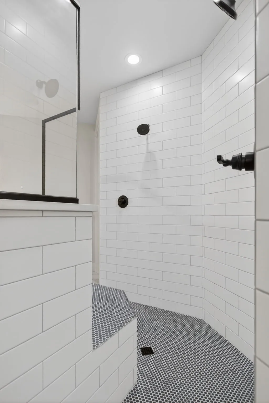 Spacious walk-in shower featuring white subway tile walls, a built-in bench with mosaic tile, and dark circular mosaic floor tiling